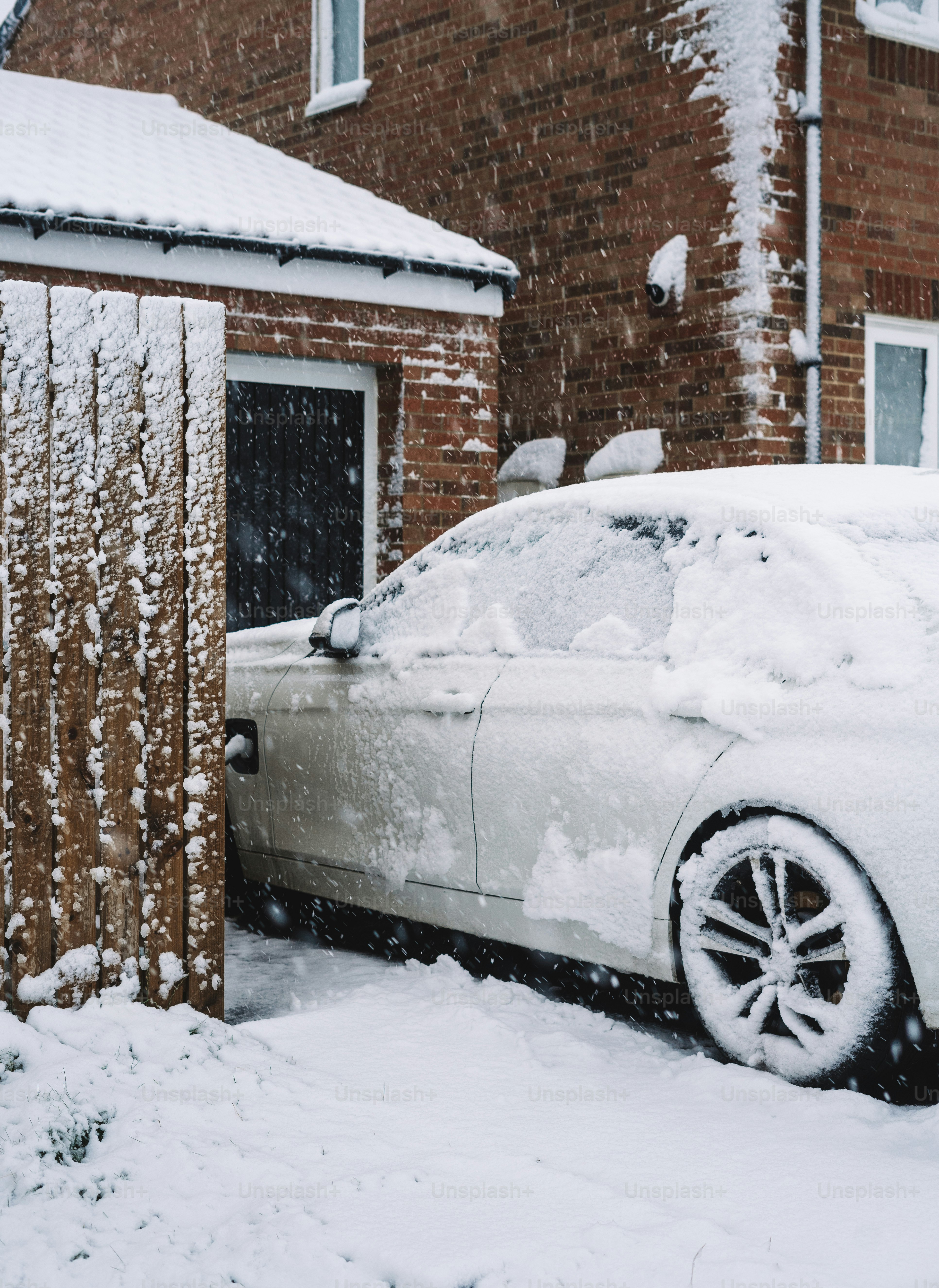A white car parked in front of a house covered in snow