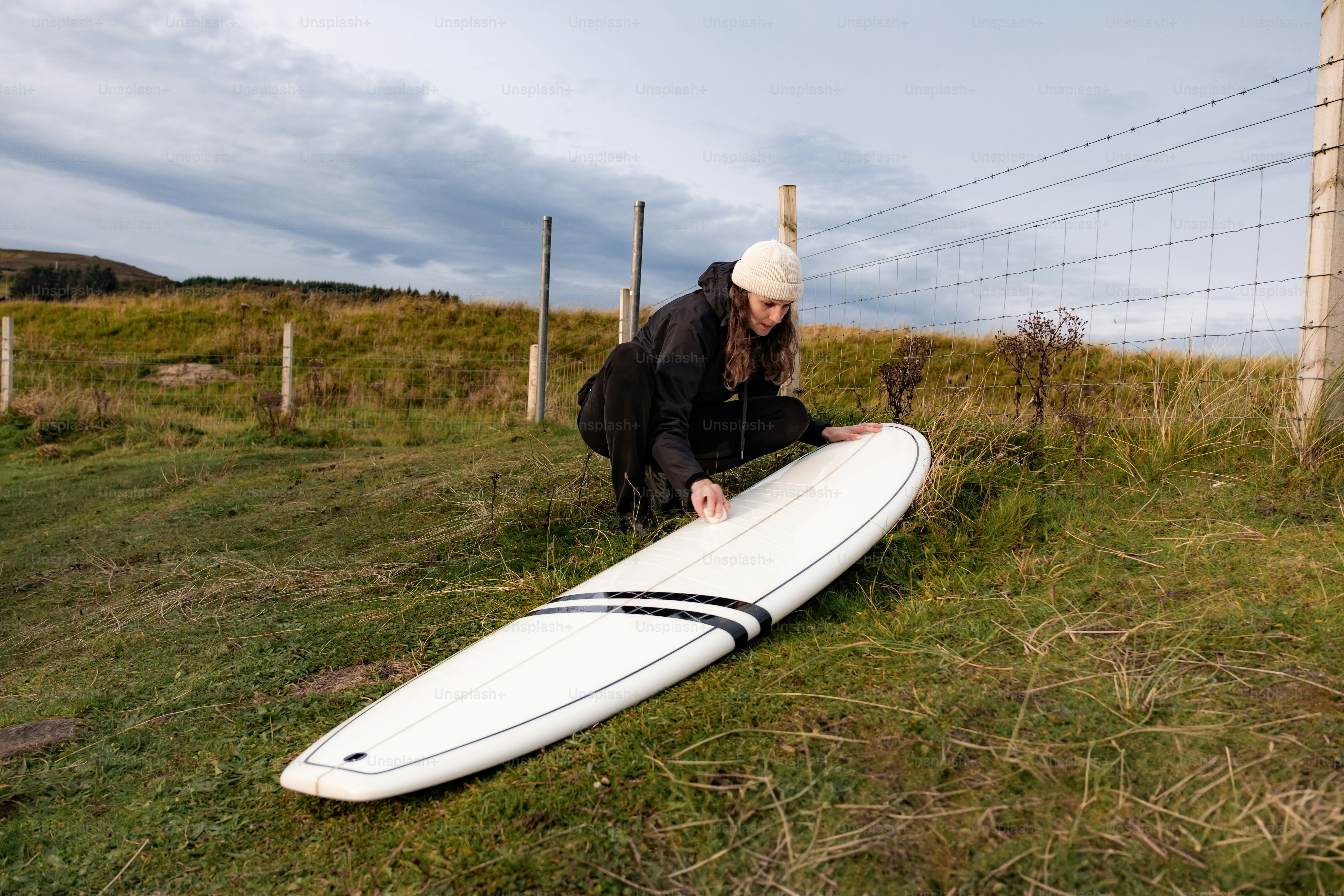 A person kneeling down next to a surfboard