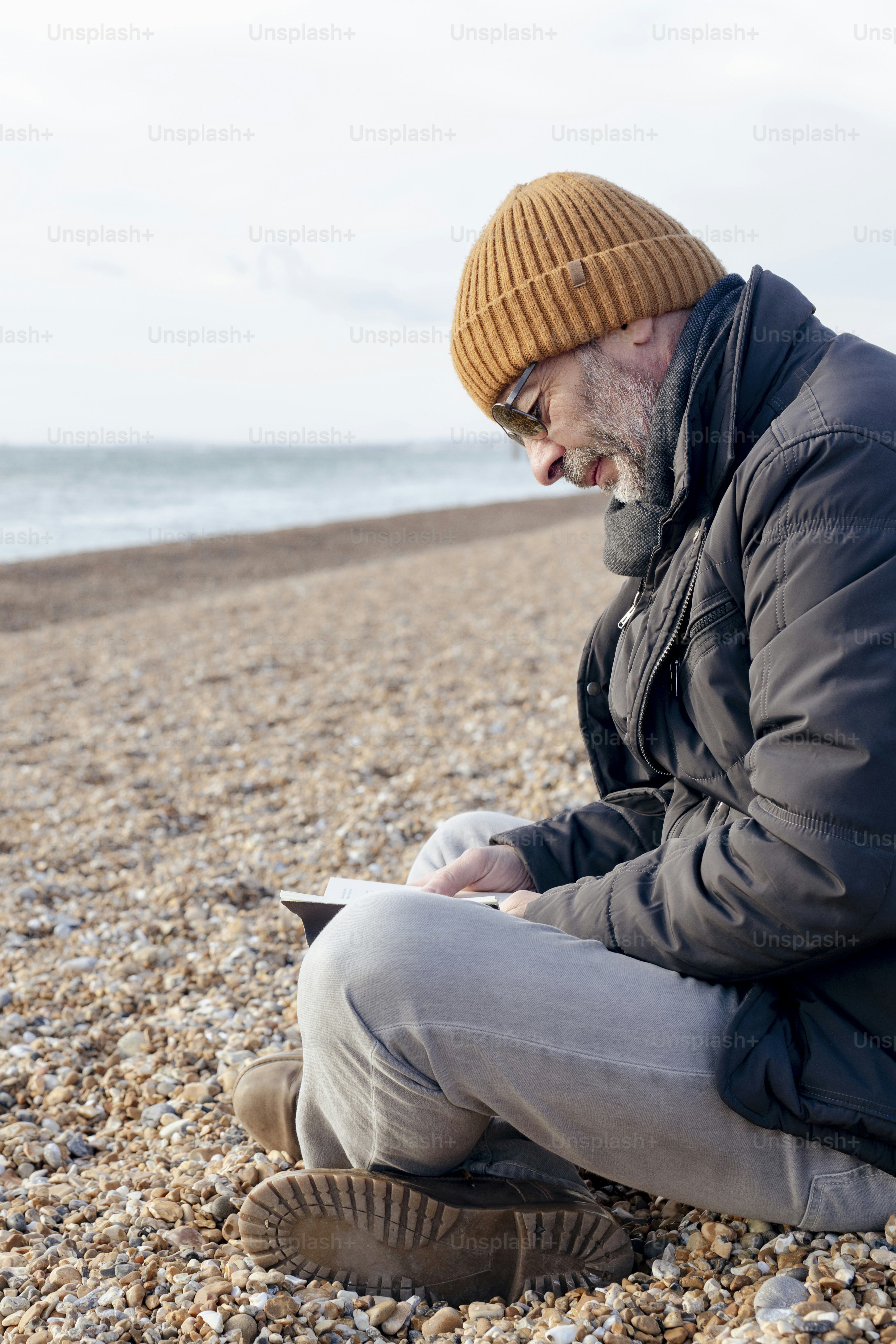 Un hombre sentado en una playa mirando su teléfono móvil