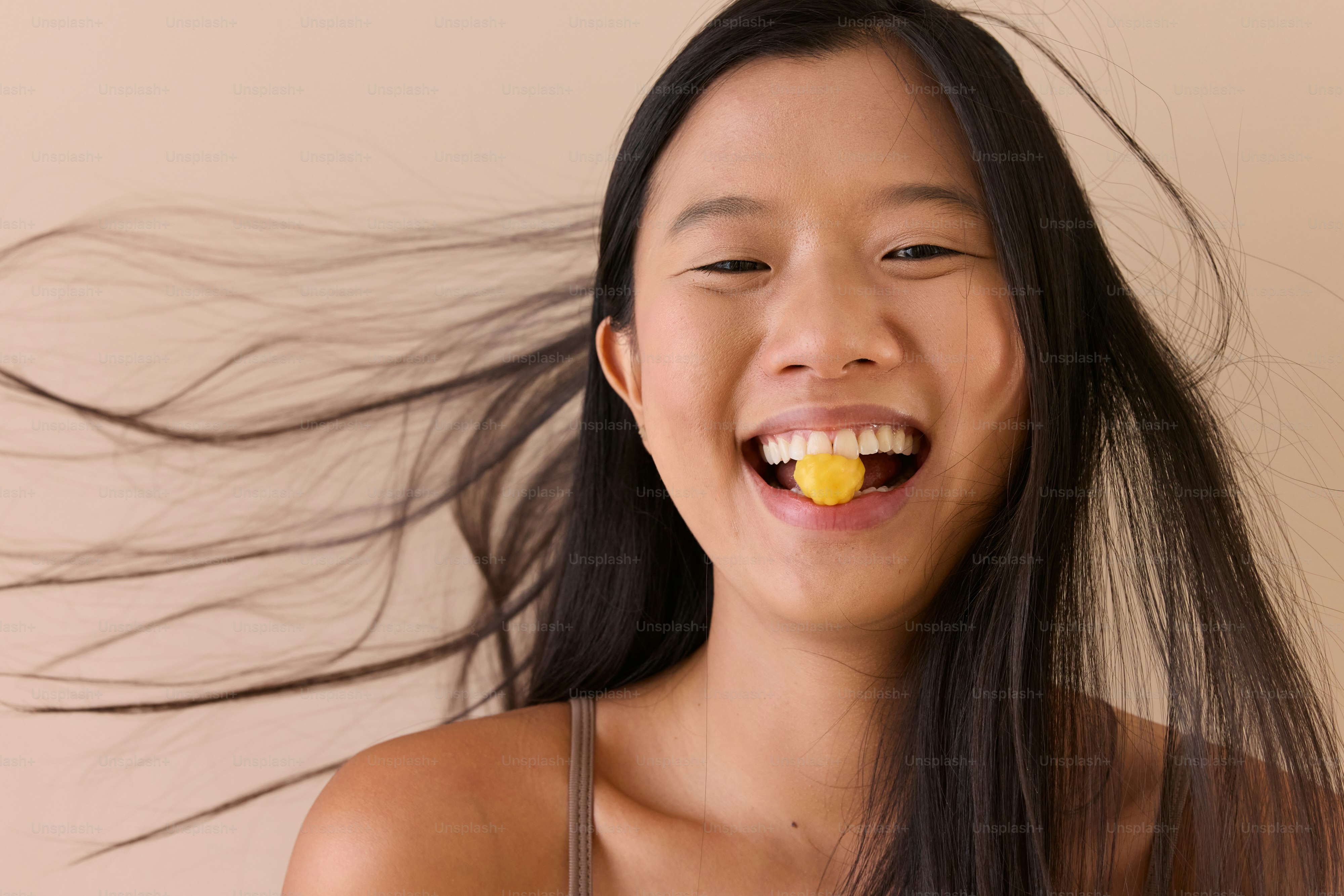 Une femme aux cheveux longs sourit et tient un fruit dans sa bouche