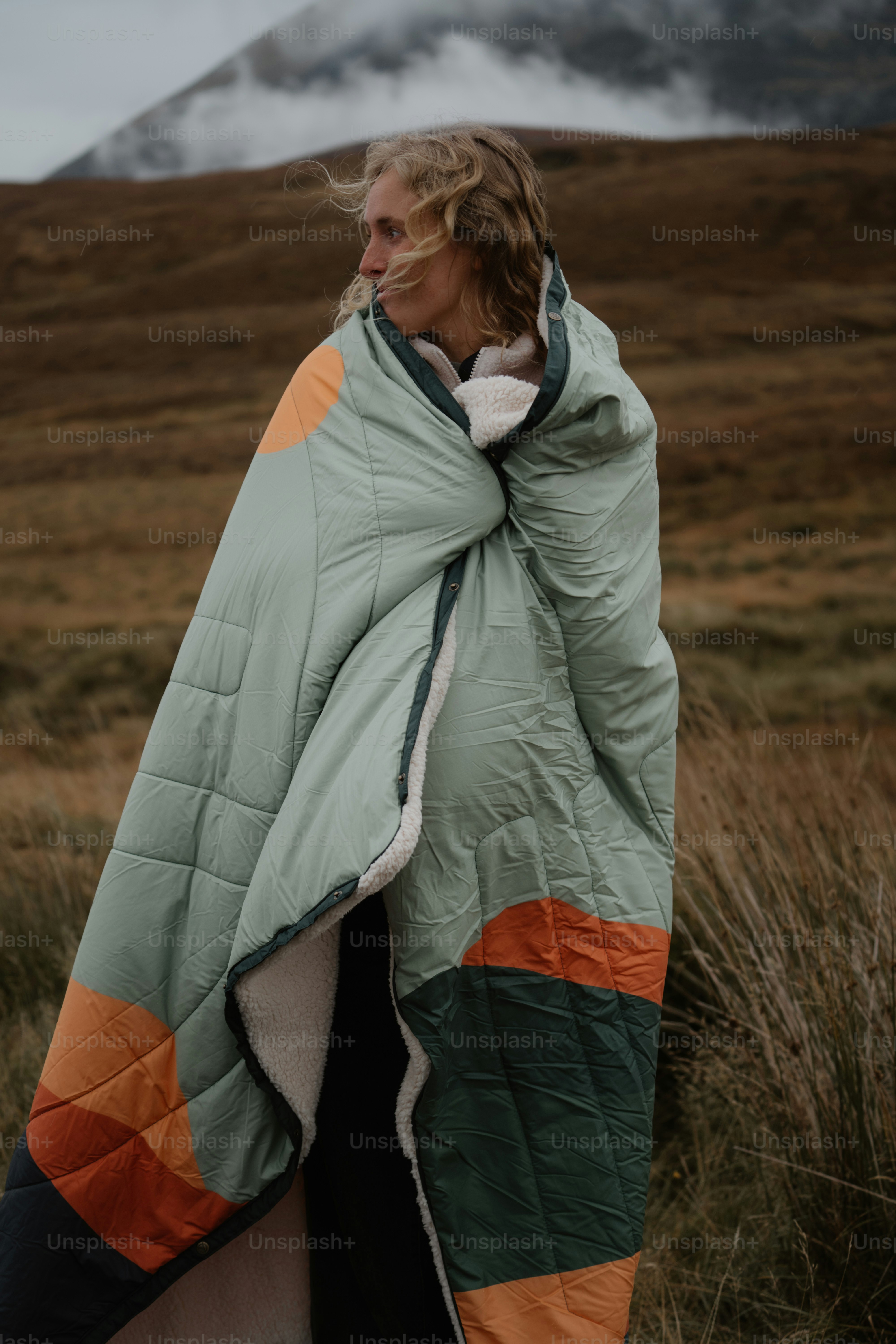 초록색과 주황색 담요를 두르고 들판에 서 있는 여자