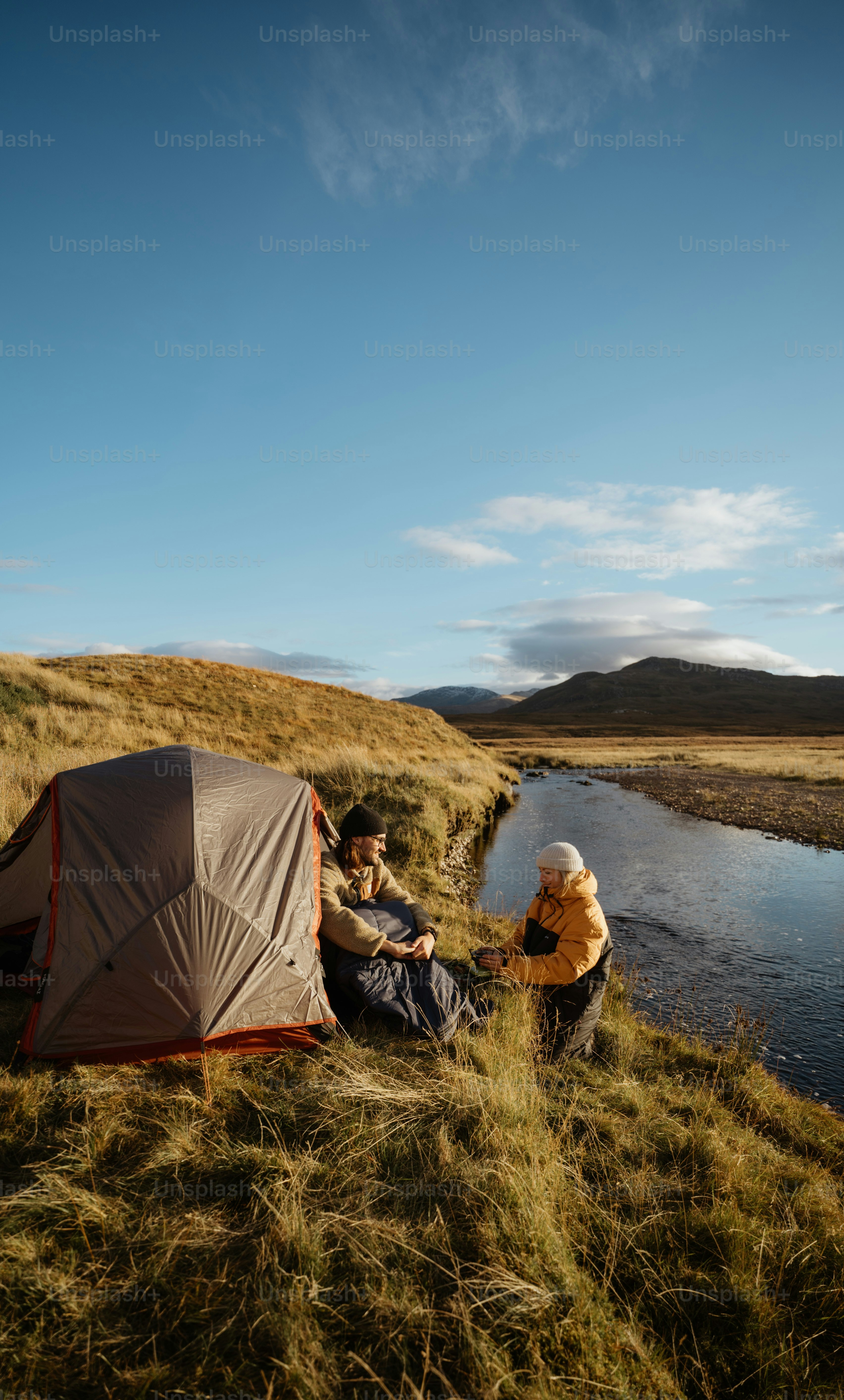 A man and a woman setting up a tent next to a river