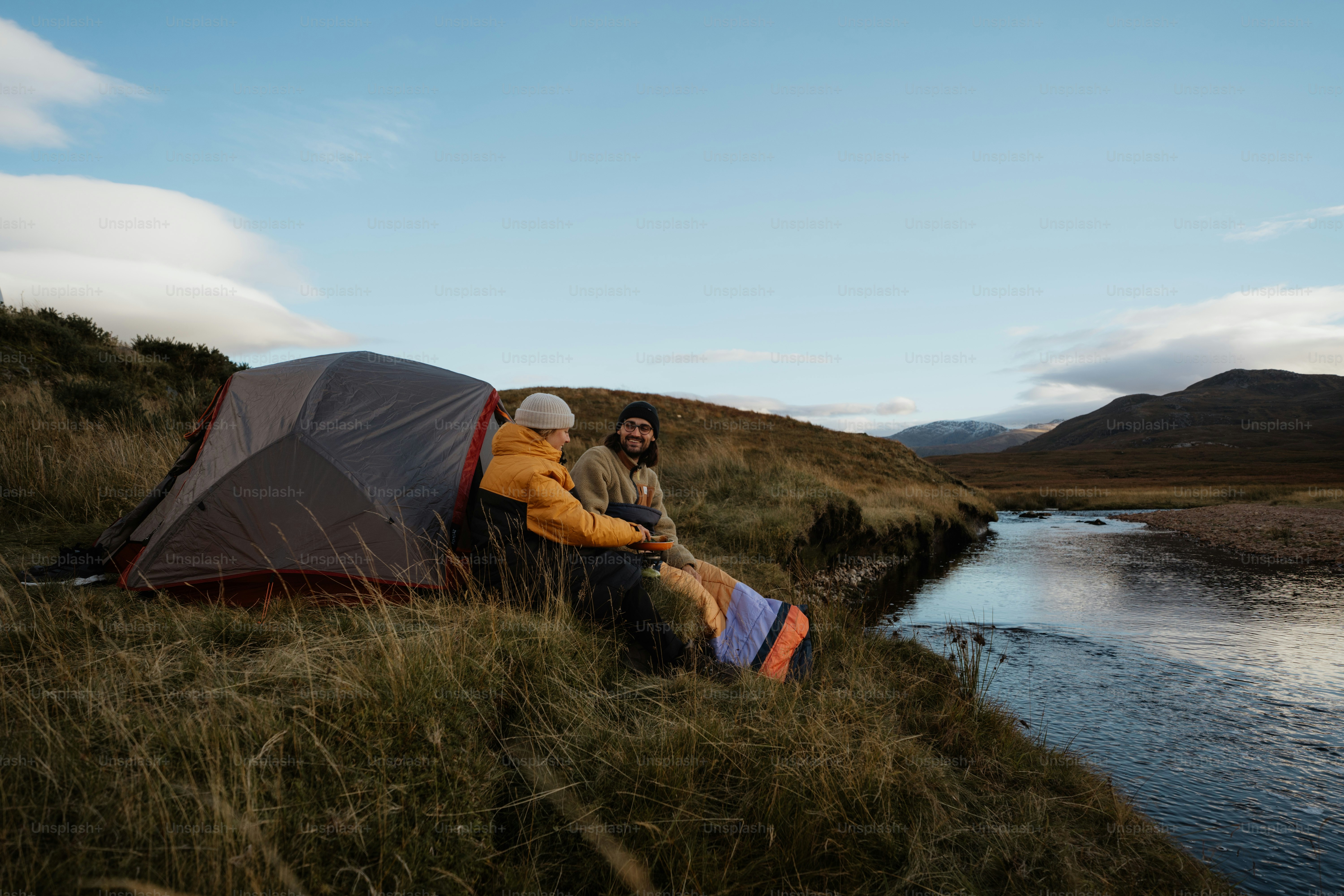 A couple of people sitting next to a tent near a body of water