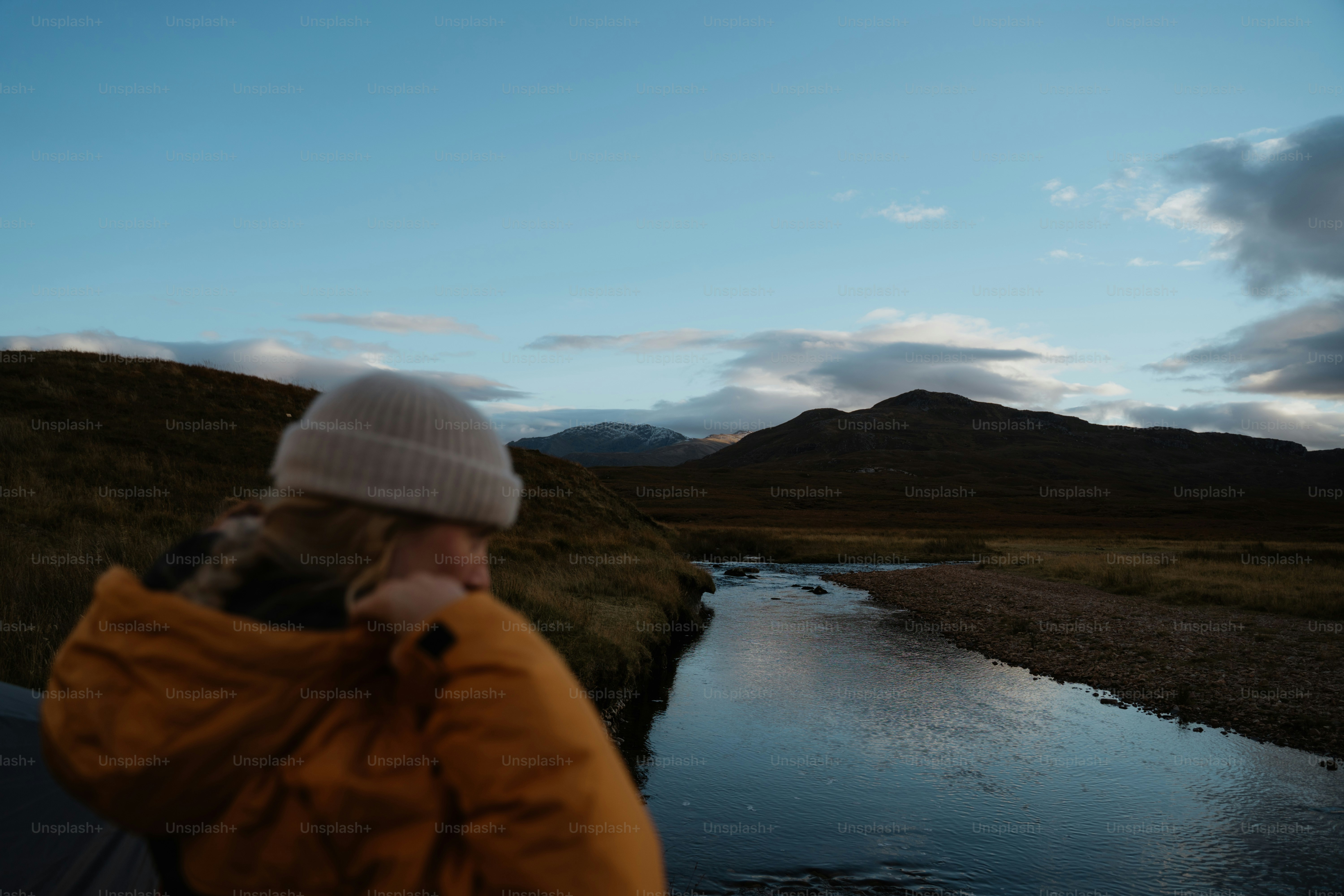 A person standing next to a river talking on a cell phone