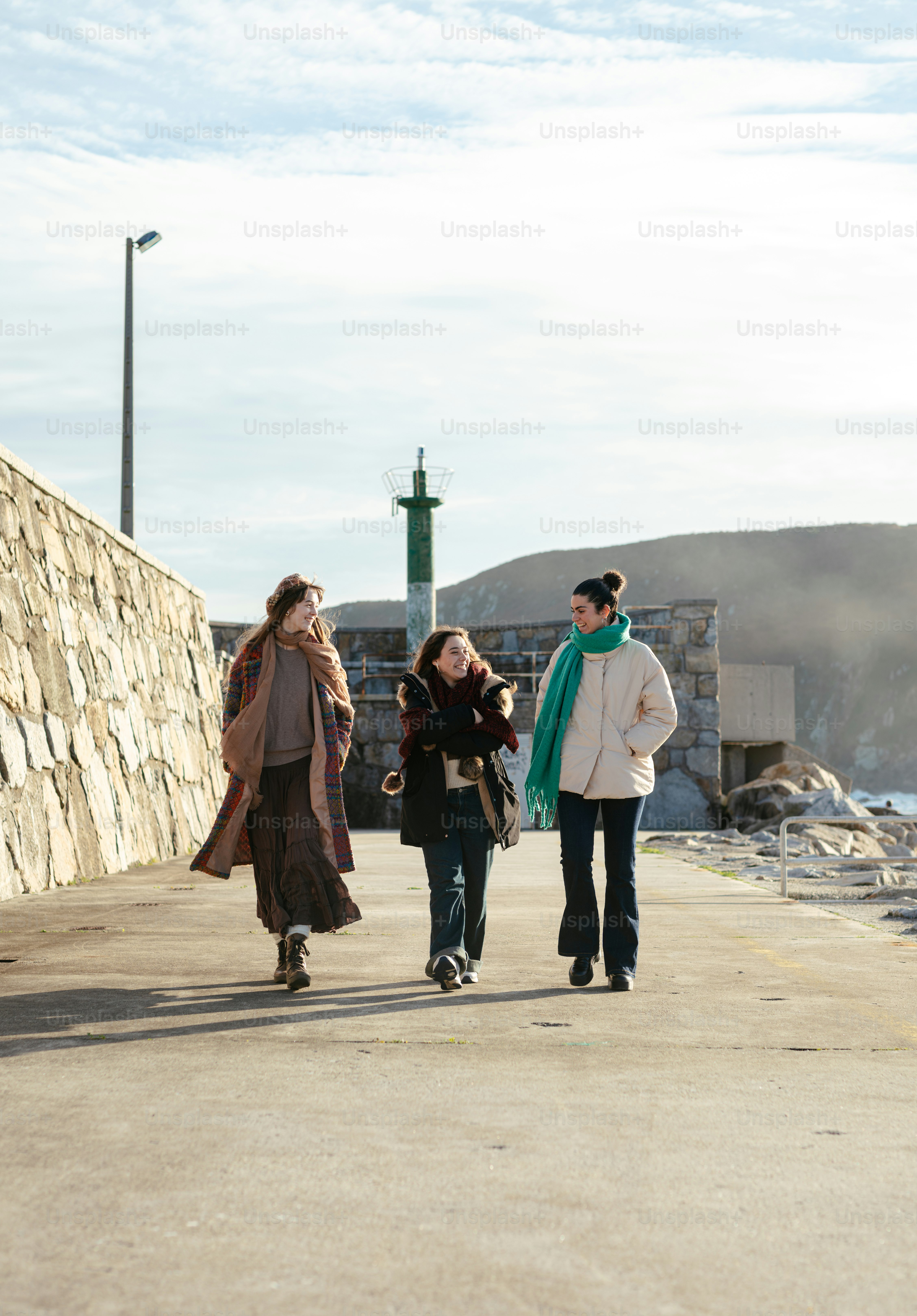 A group of people walking down a street next to a stone wall