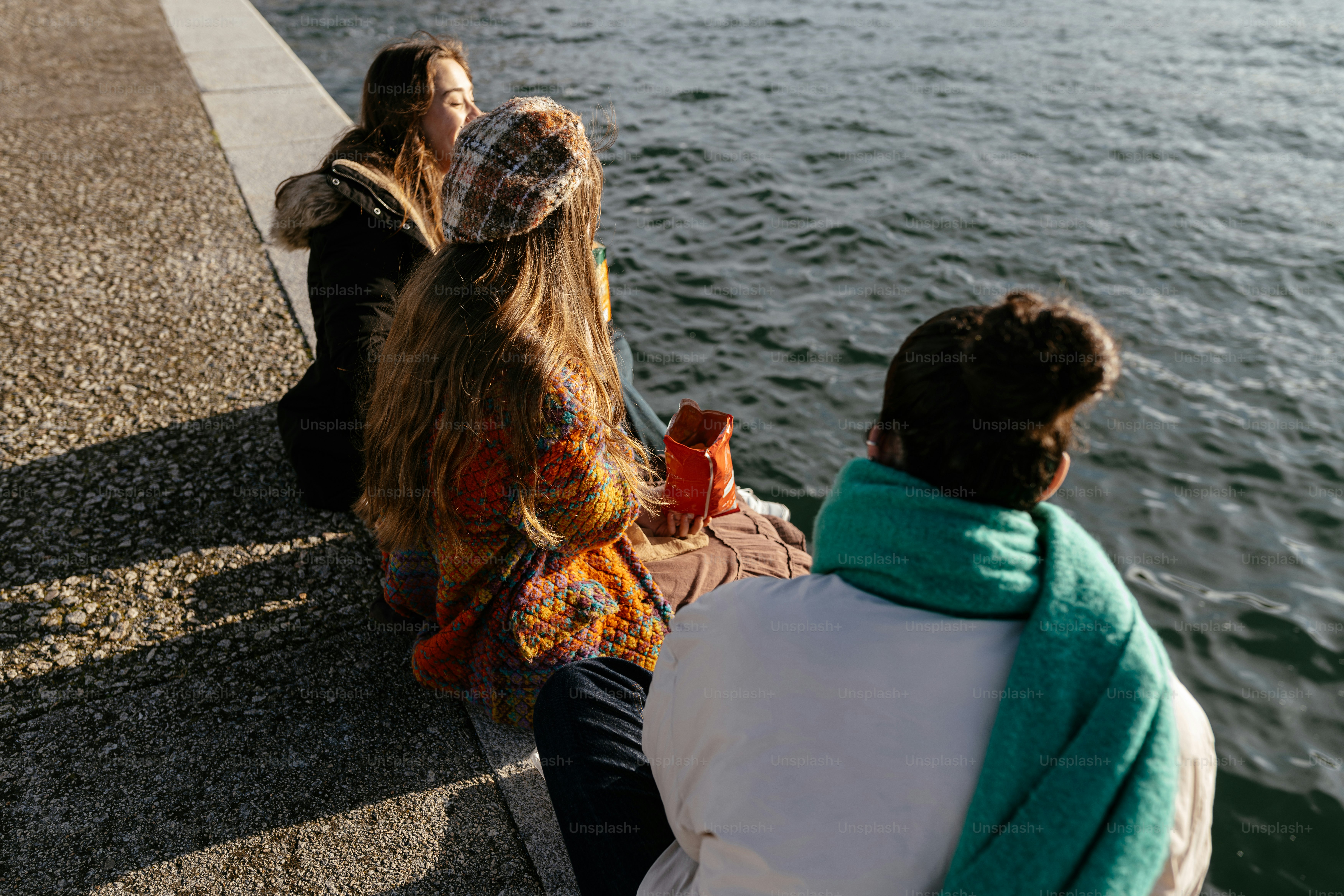 A group of people sitting next to a body of water photo – Beach Image ...