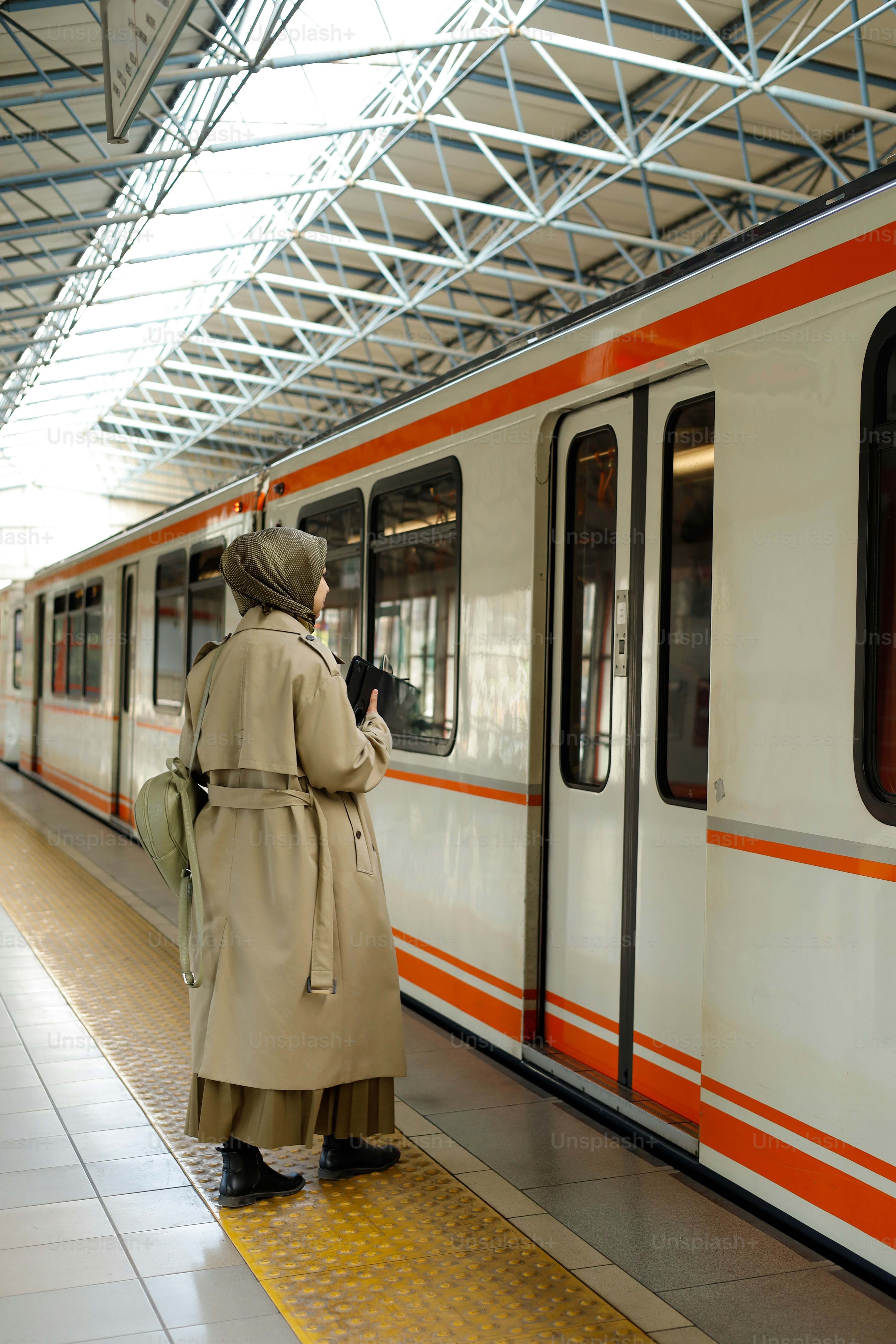A woman in a trench coat waiting for a train