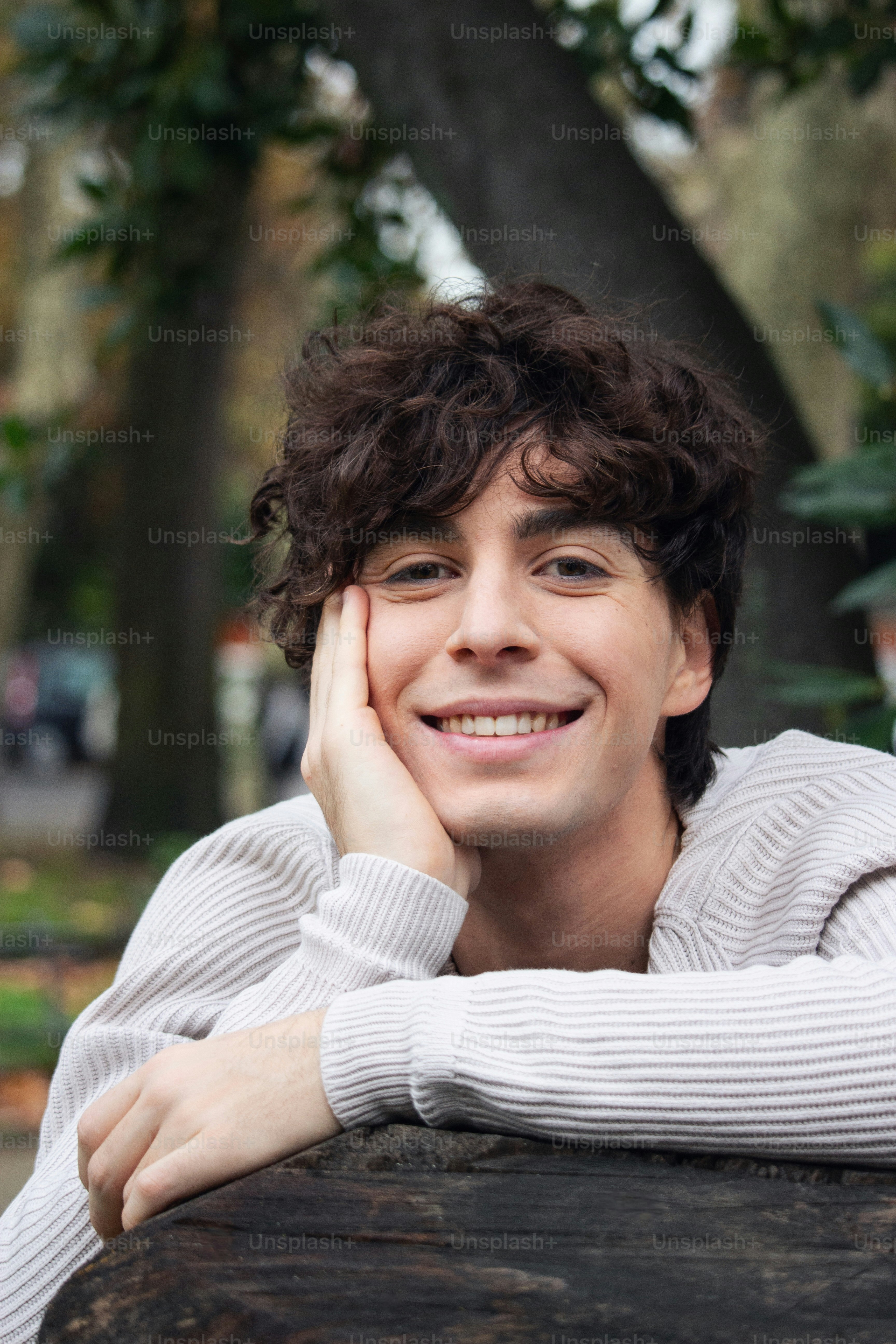 A smiling young man leaning on a tree trunk