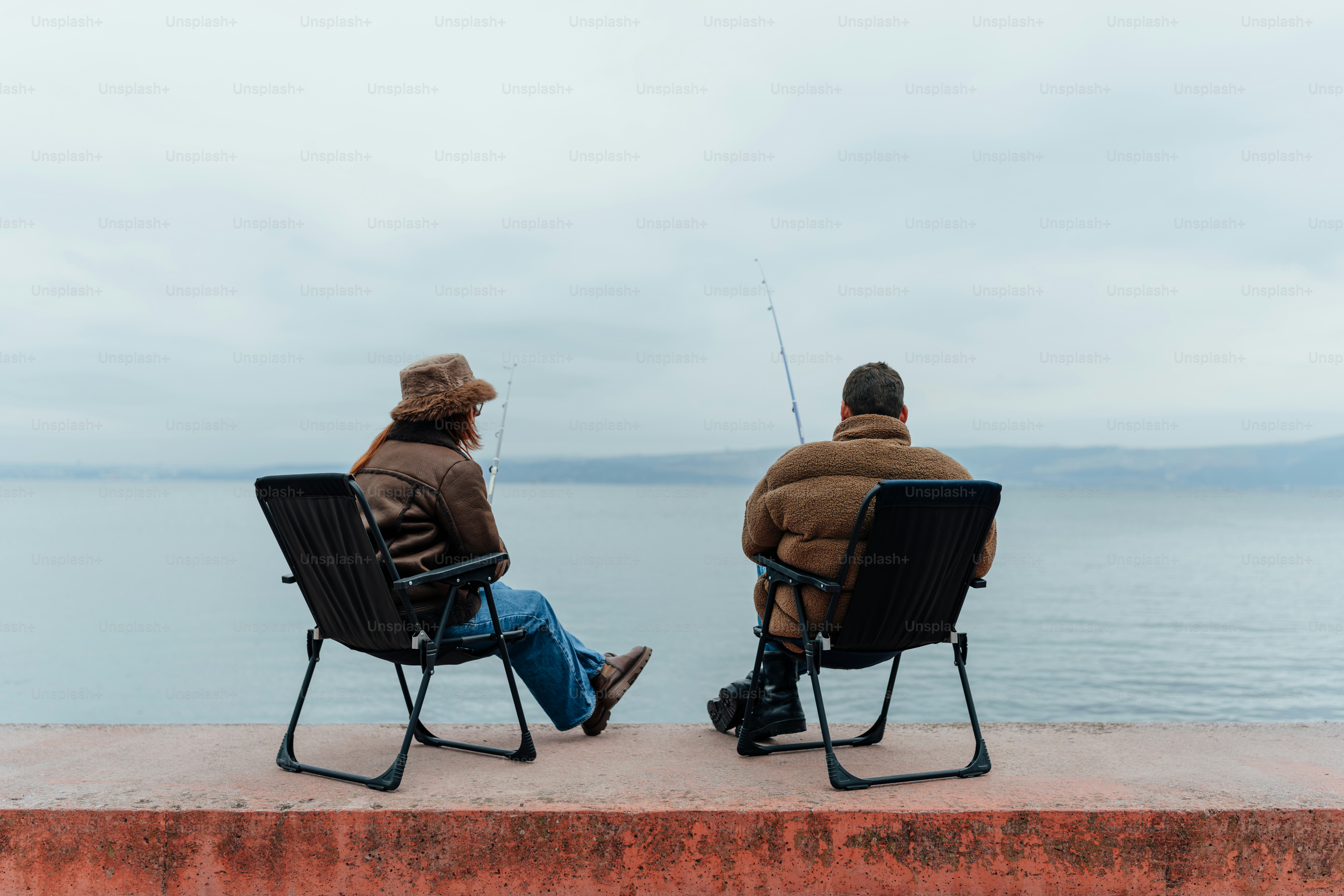 Two people sitting in chairs facing the water