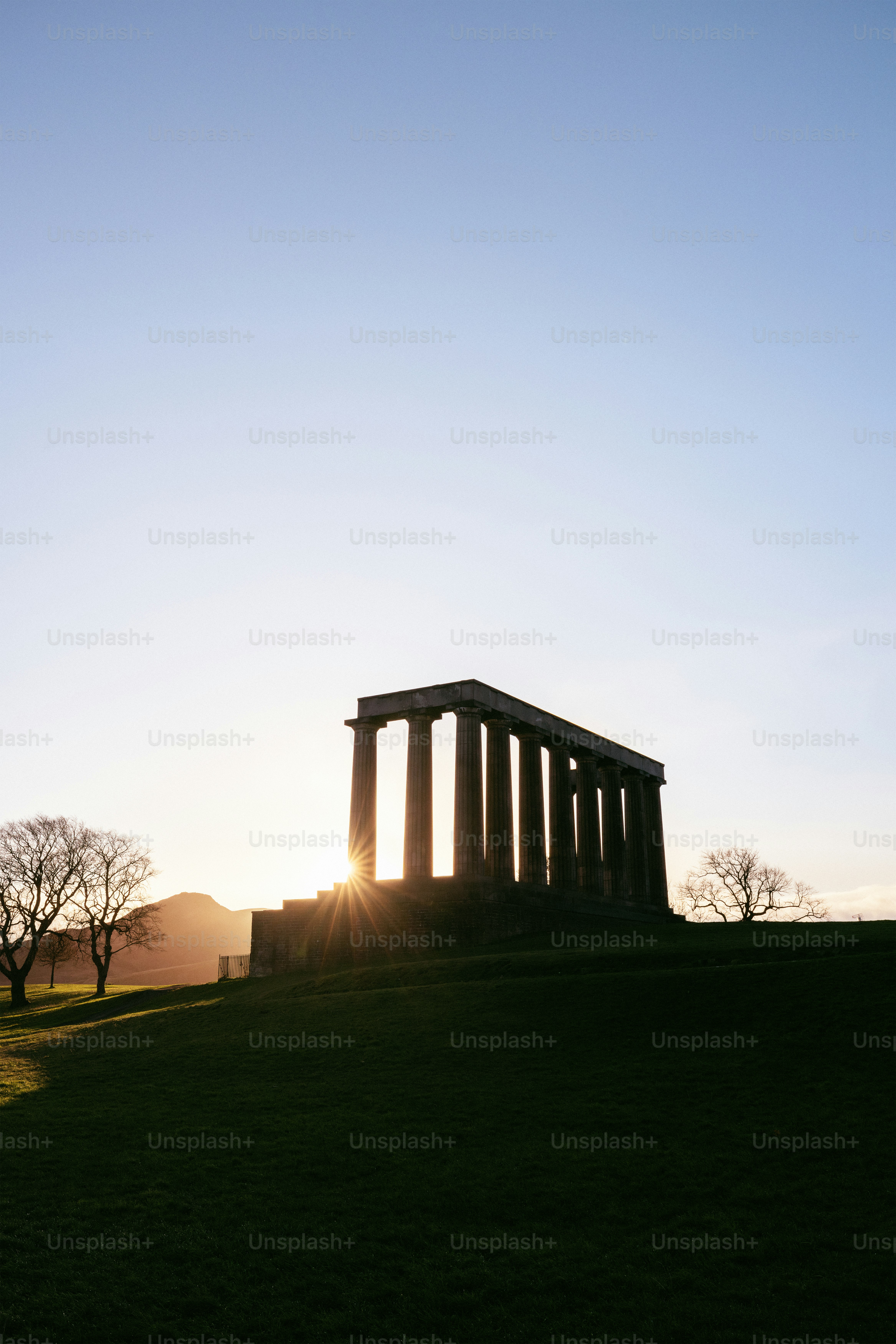 The sun is setting behind a monument on a hill