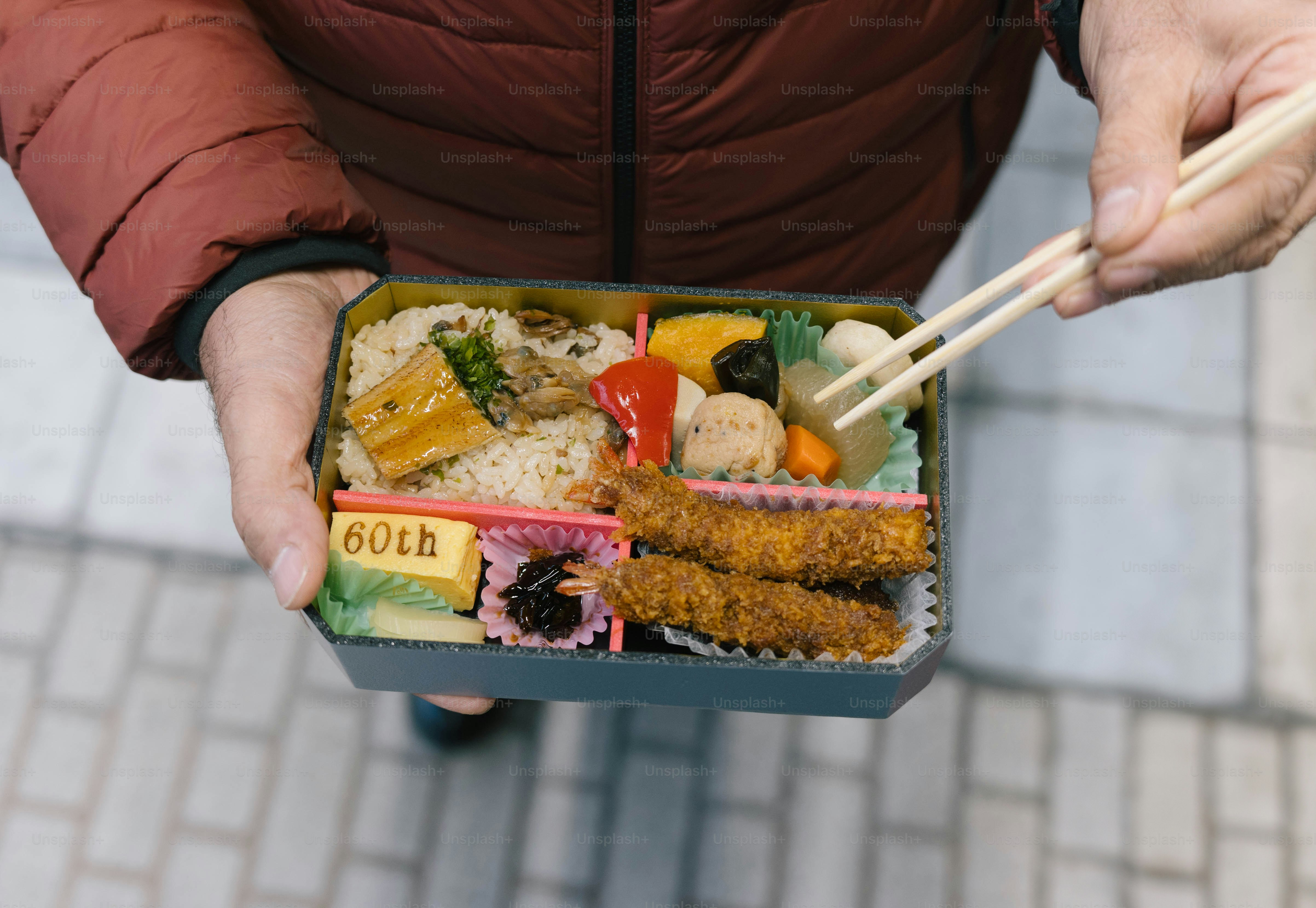 A person holding a box of food with chopsticks