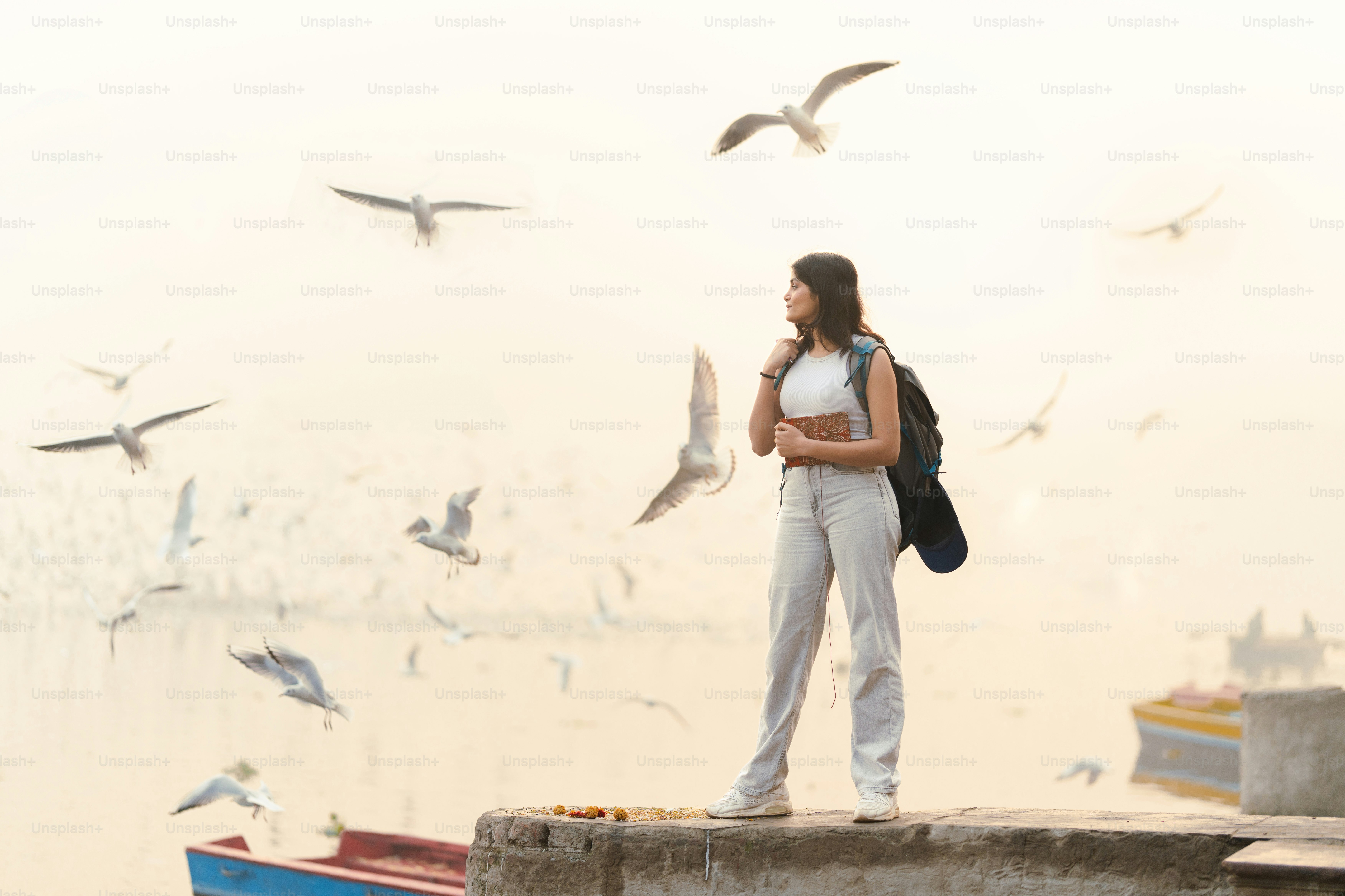 A woman standing on a dock with birds flying around her photo – Indian ...