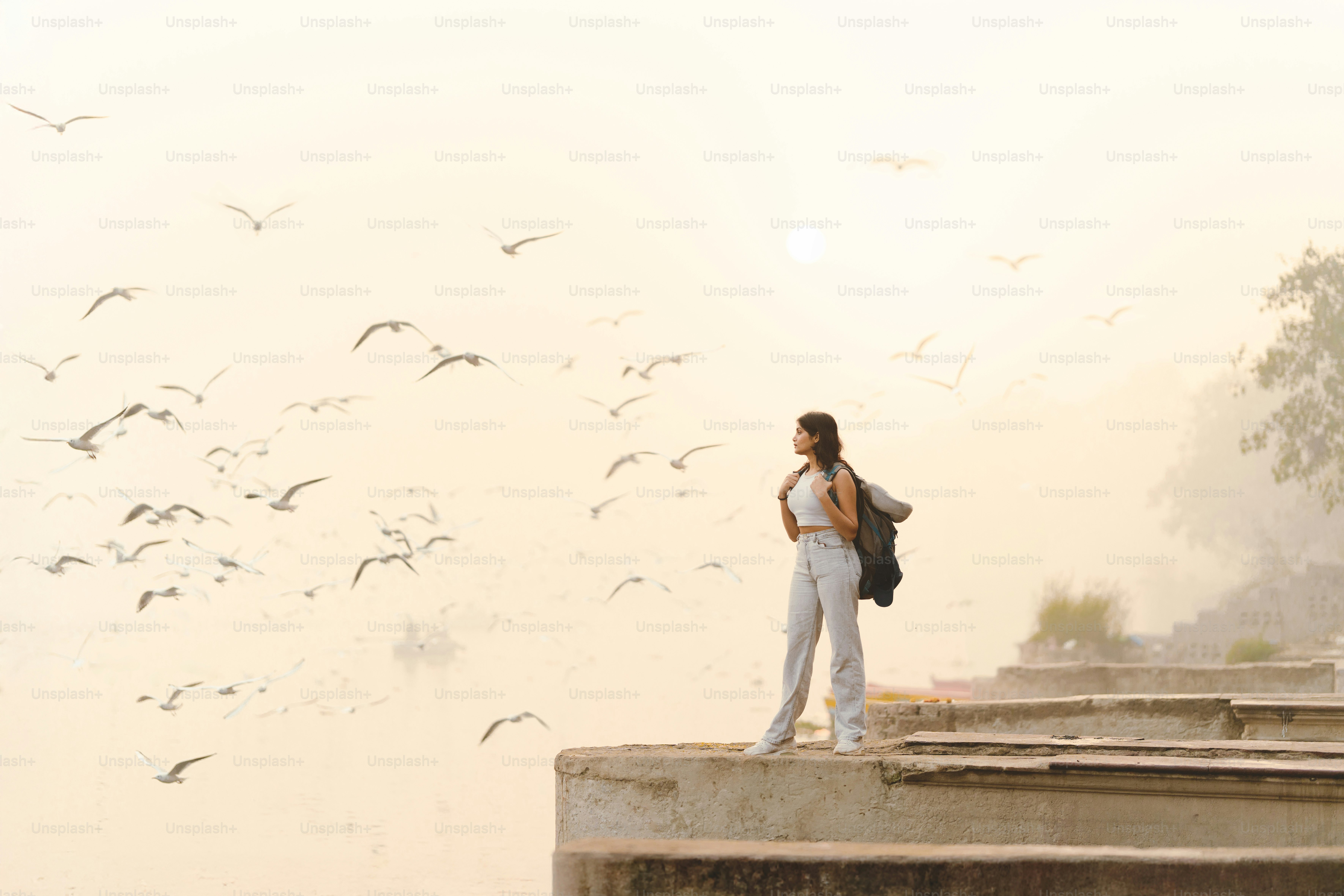 A woman standing on a ledge with a flock of birds in the background