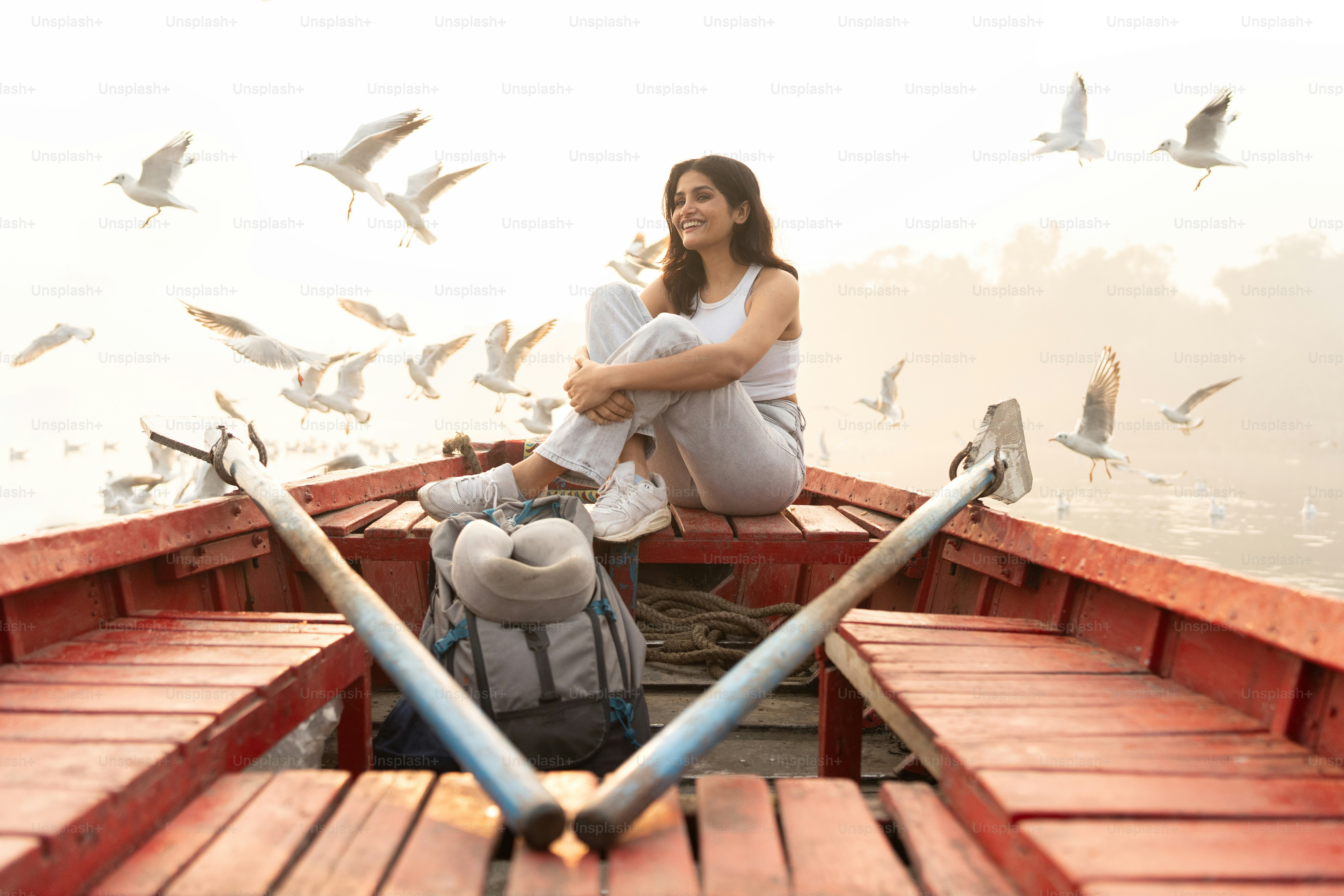 Una mujer sentada en un bote con pájaros volando a su alrededor