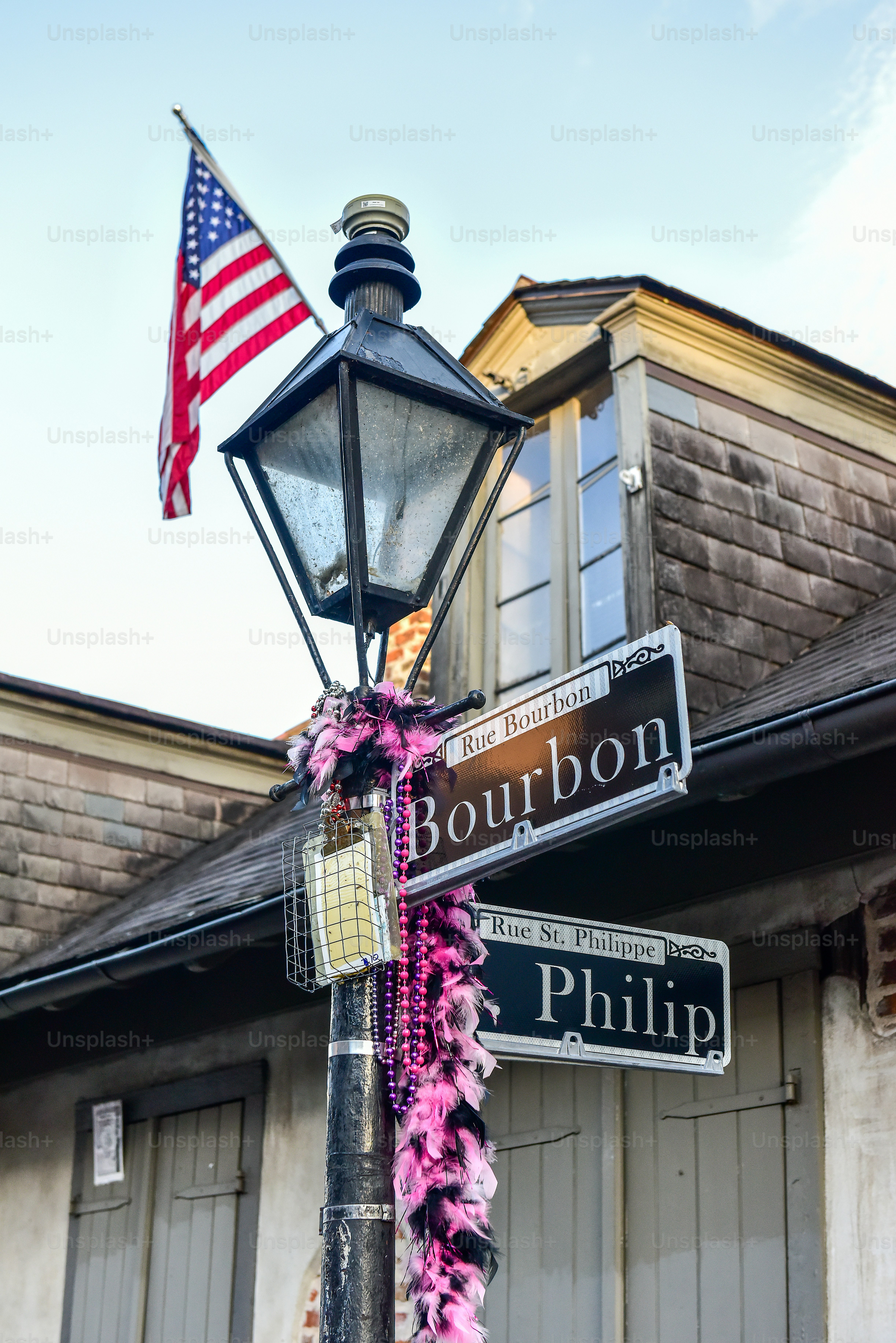 Bourbon Street lamppost, adorned with colorful necklaces and a small American flag, in the French Quarter of New Orleans.
