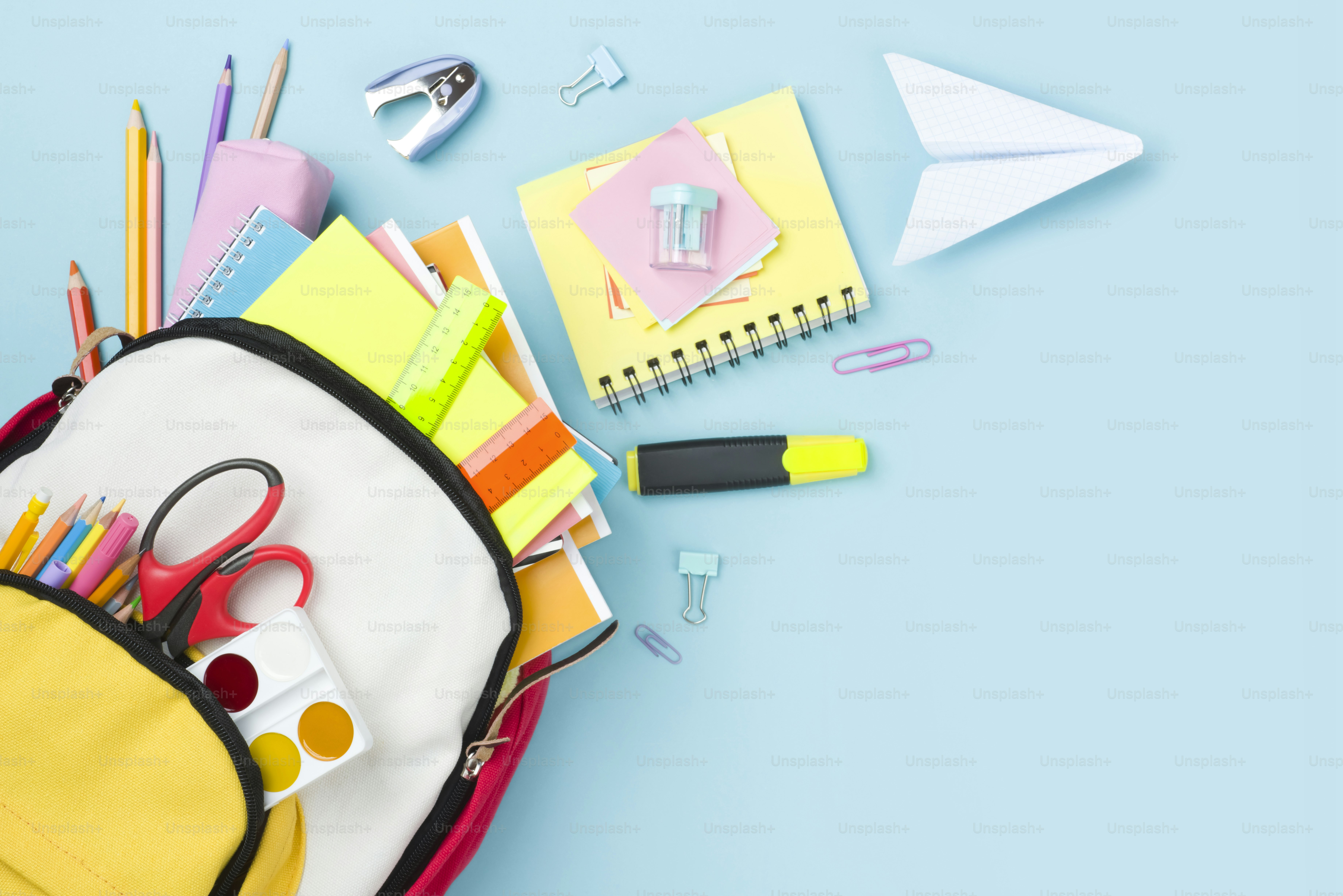 Many colorful school supplies and backpack arranged on blue background