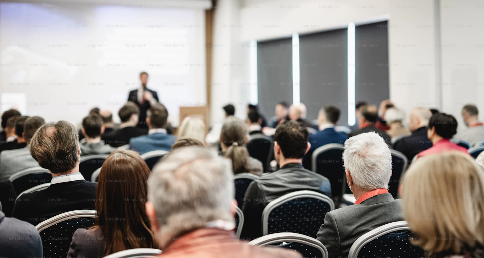 Conference attendees seated before a large display screen