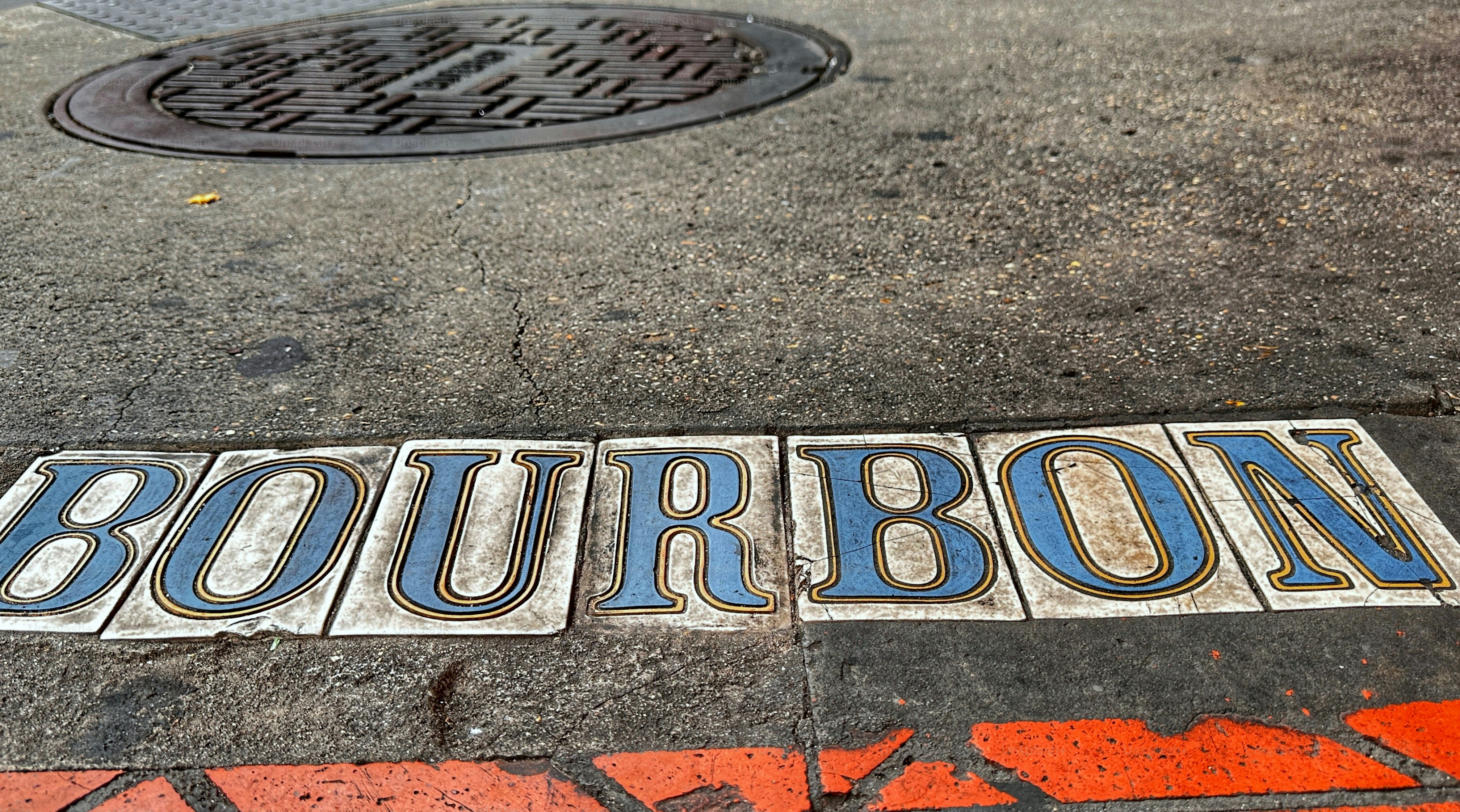Surface level view ceramic tiles of famous street on sidewalk. Location signage near manhole. French Quarter, New Orleans, Louisiana, USA.