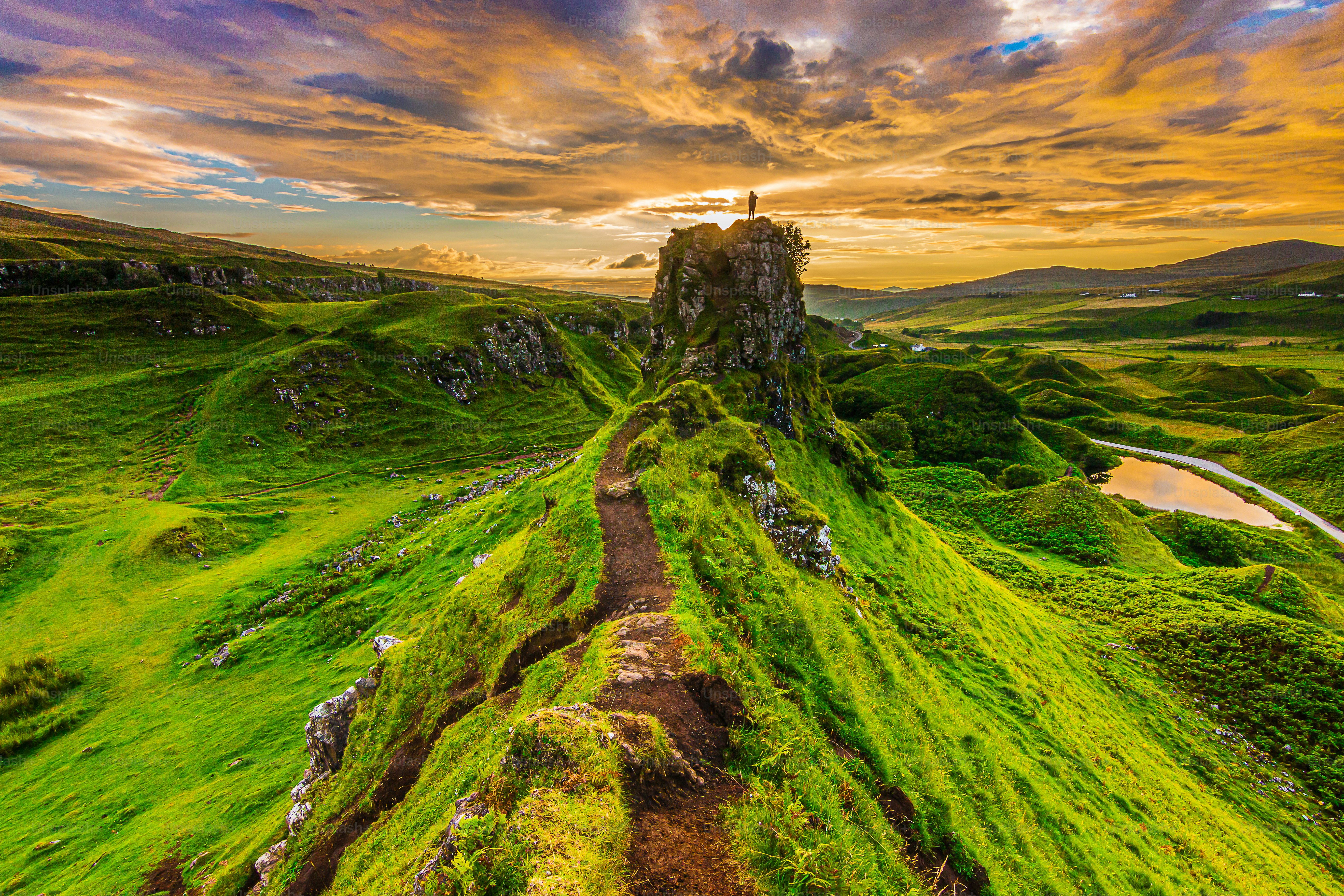Sunset on the Isle of Skye in summer with Castle Ewen rock and a silhouette of a person at the top. Landscape in Scotland in the evening with clouds in the sky. path on the cliff edge