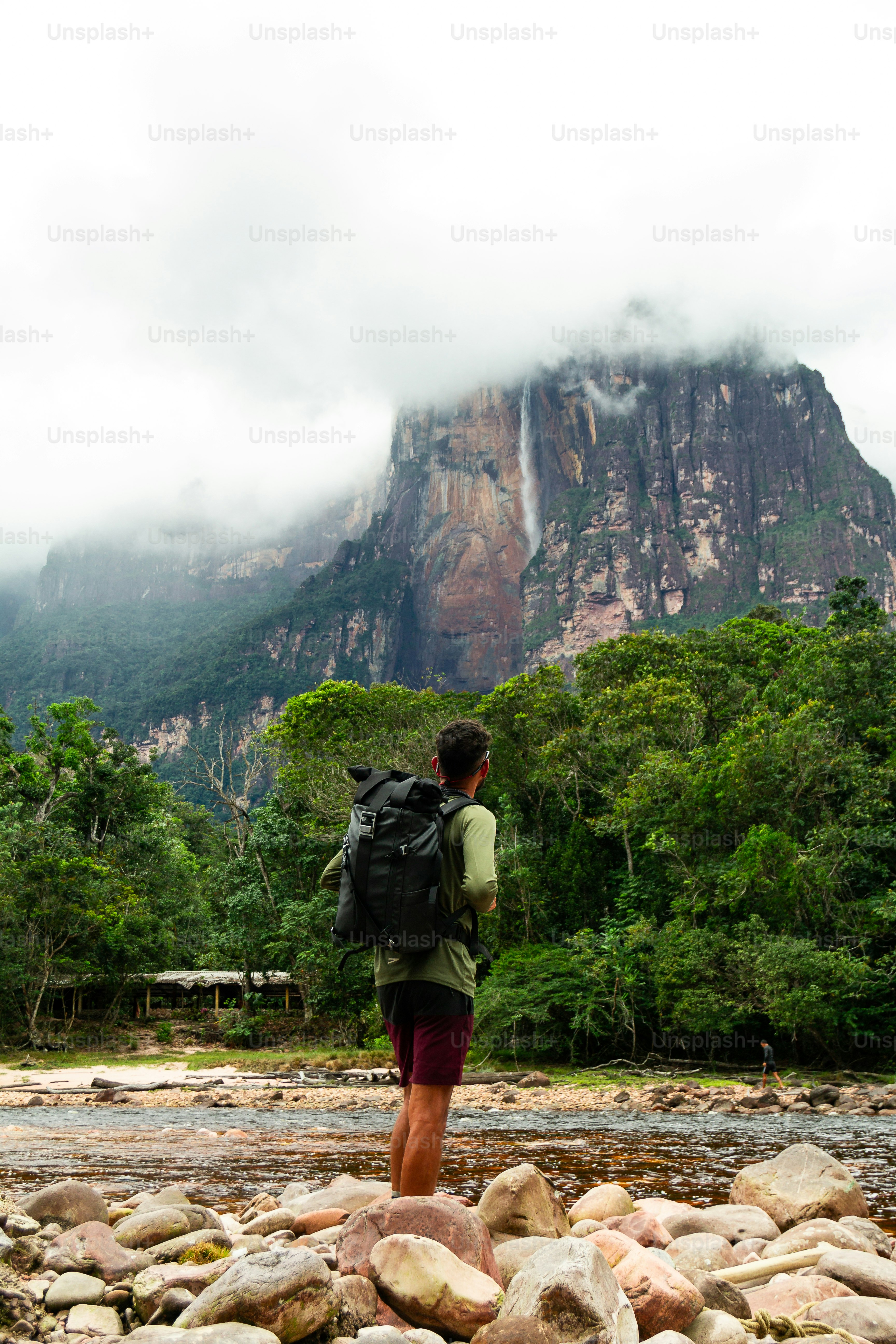 young adult latin-hispanic person with green long-sleeve shirt, glasses and backpack looking at Angel Falls from Isla Ratón. Highest waterfall in the world (979m) in Canaima National Park, Venezuela