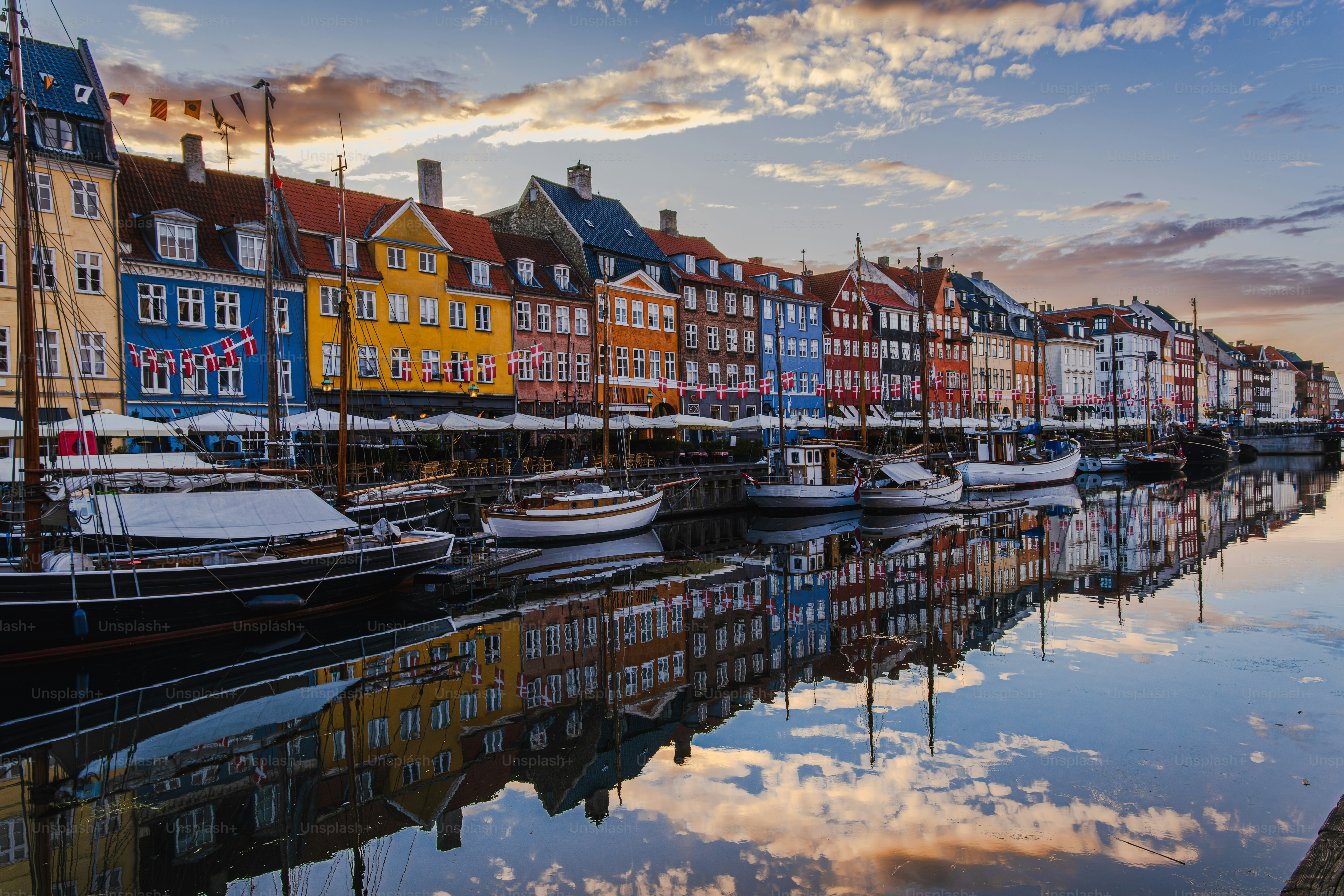 View of Nyhavn canal area in Copenhagen, Denmark, at sunrise; colorful buildings reflecting in calm water