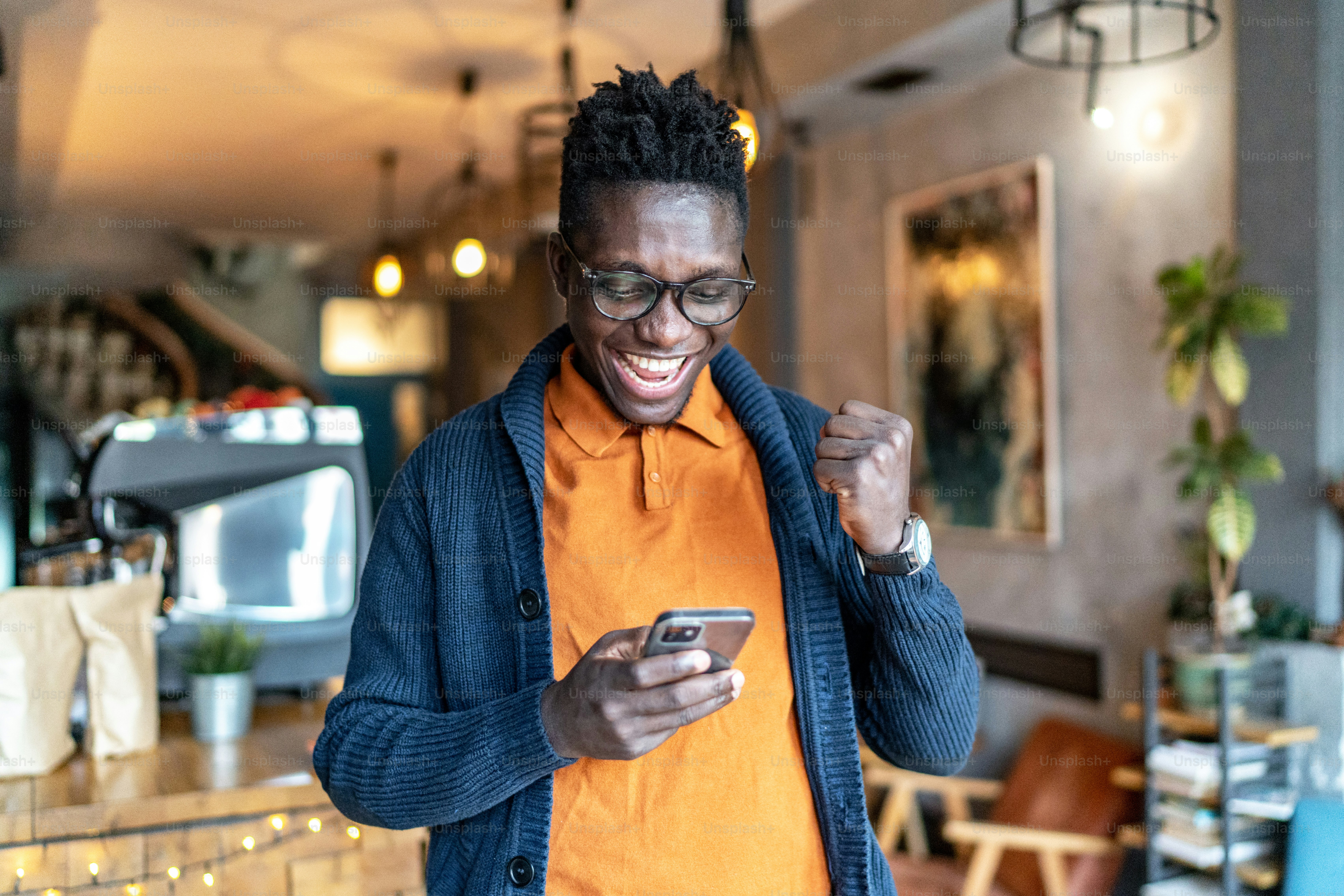 Handsome young man screaming and cheerfully pumping fist while reading good news over smart phone