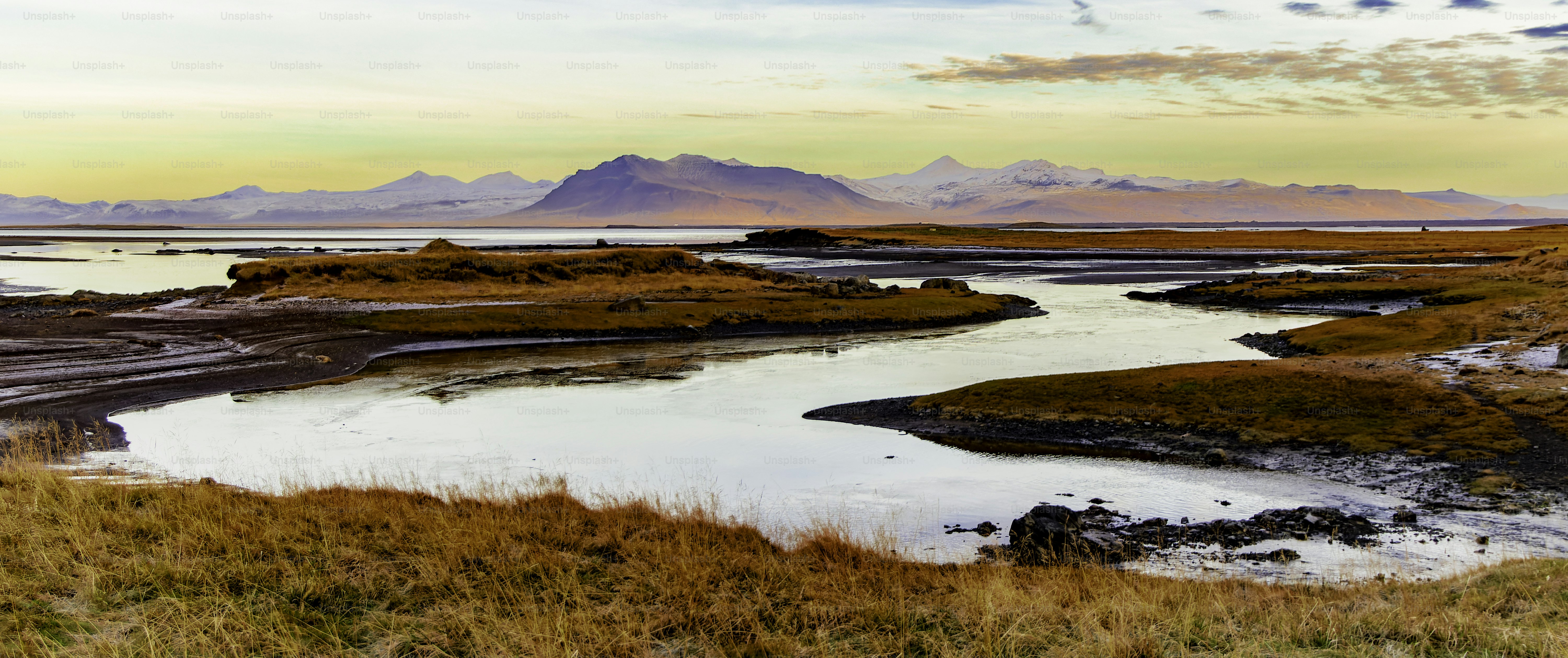 Un paysage magnifique traversé par une rivière. L’eau est calme et le ciel est un mélange d’orange et de bleu. La scène est paisible et sereine