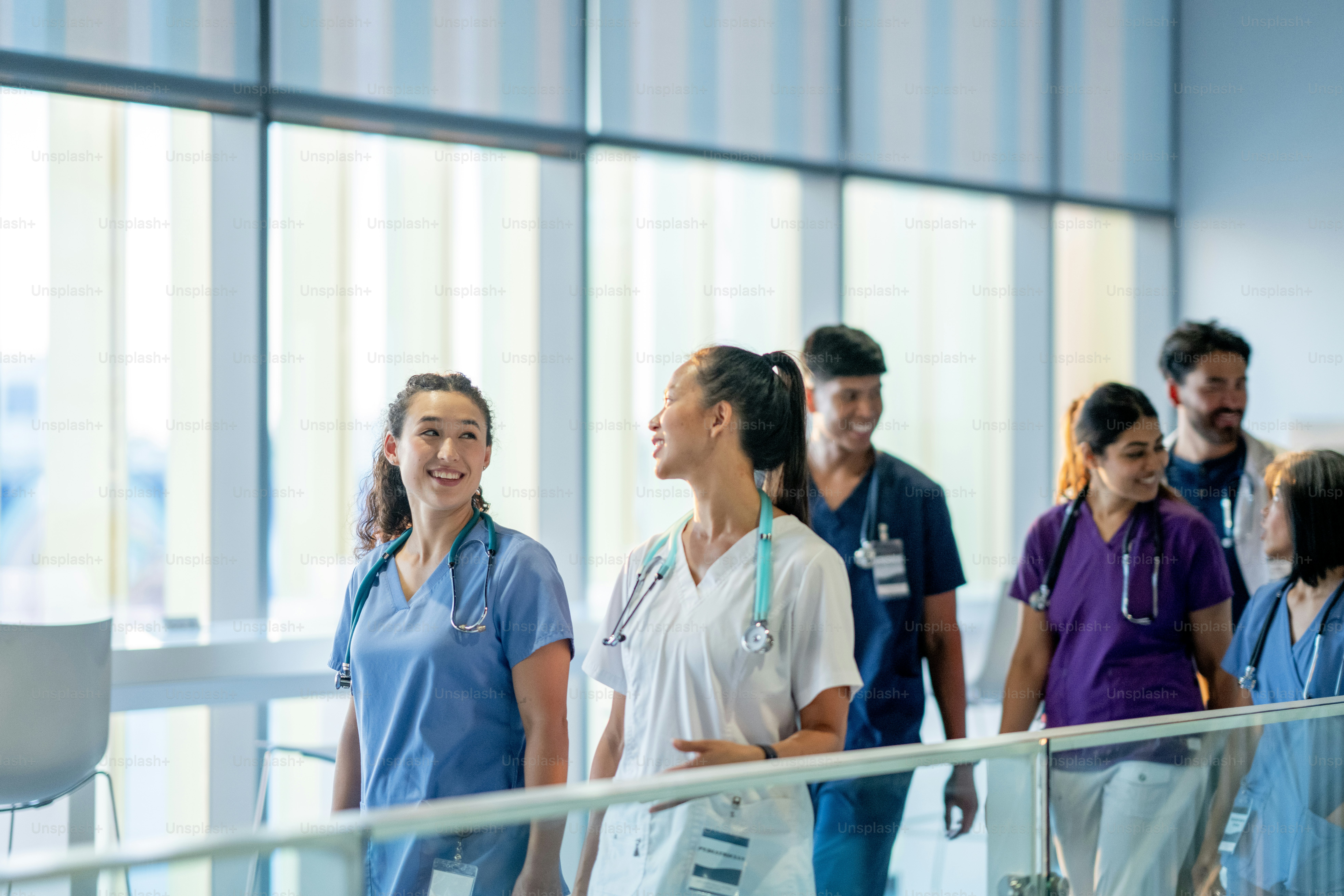 A small team of medical professional's are seen walking through the halls of a hospital as they make rounds together to patients.  They are each dressed in scrubs and are smiling as they talk amongst each other.