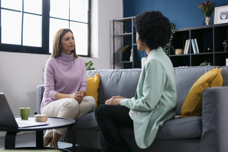 A young woman engaged in conversation with her female psychologist on a sofa during a therapy session