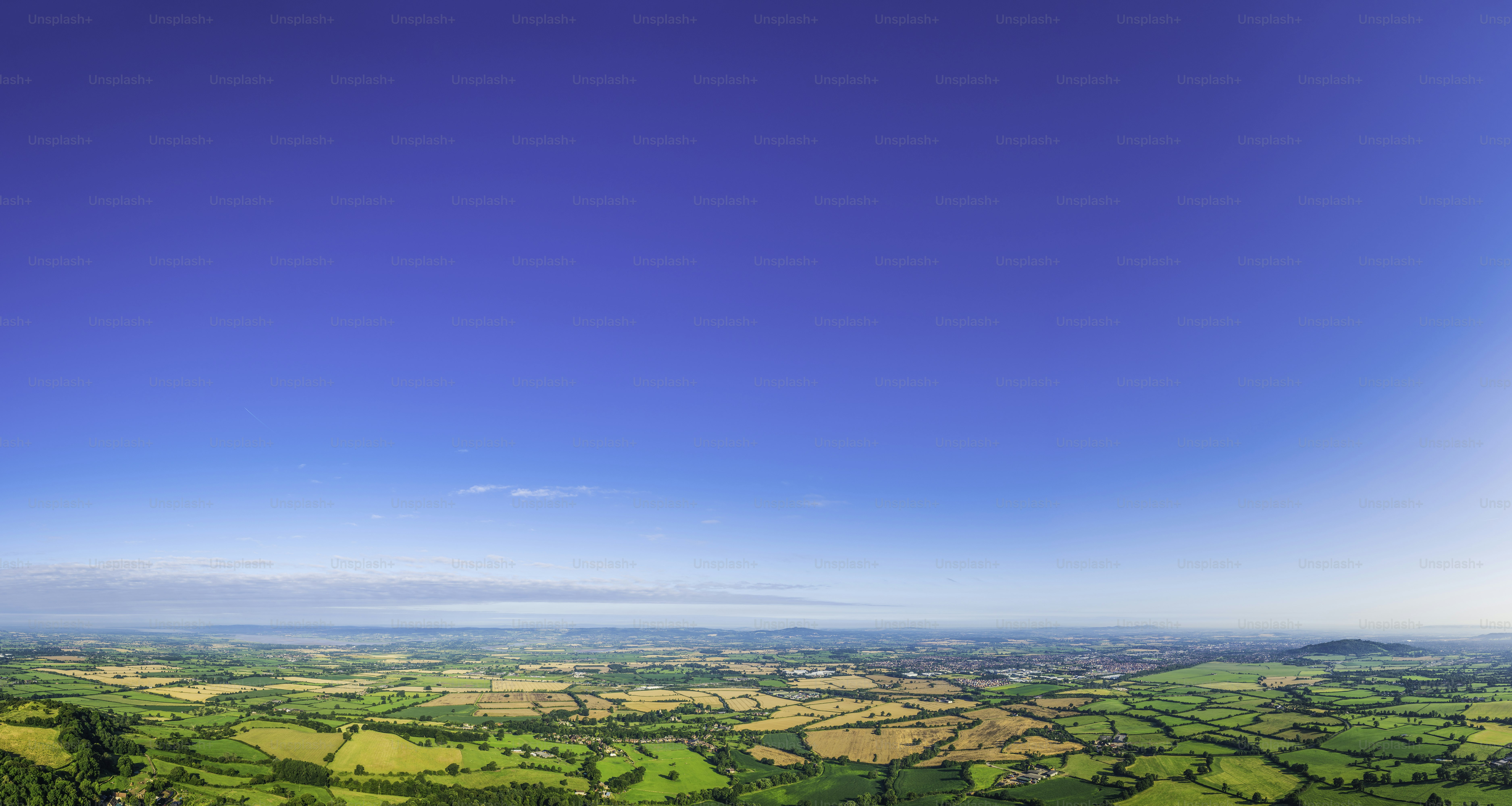 Grandes cielos azules de verano sobre un pintoresco paisaje de retazos de pastos verdes y campos de cultivo dorados, pueblos rurales, granjas y pueblos rurales. Perfil ProPhoto RGB para una máxima fidelidad de color y gama.