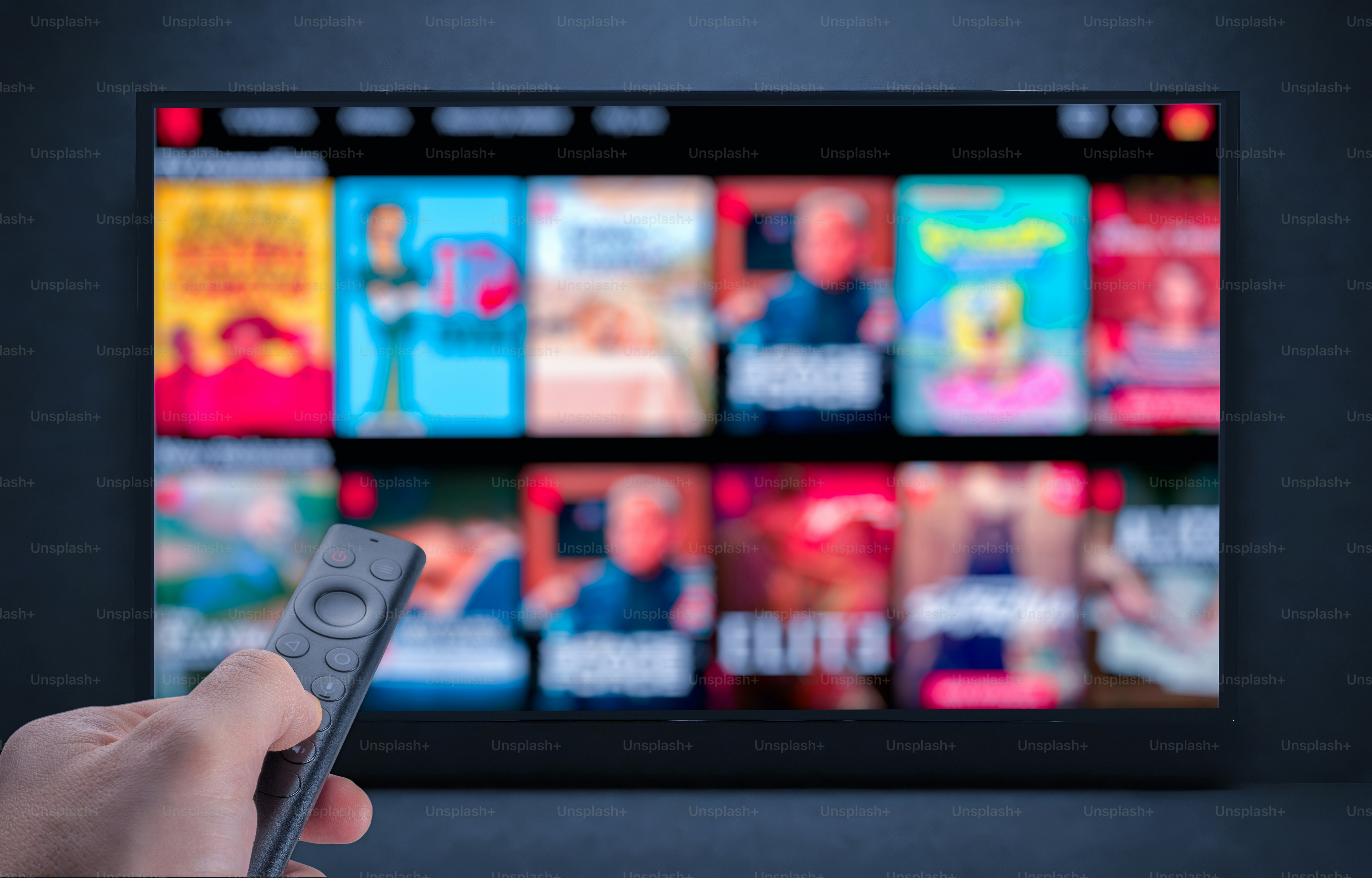 A hand holding a remote control pointed at a television screen displaying content