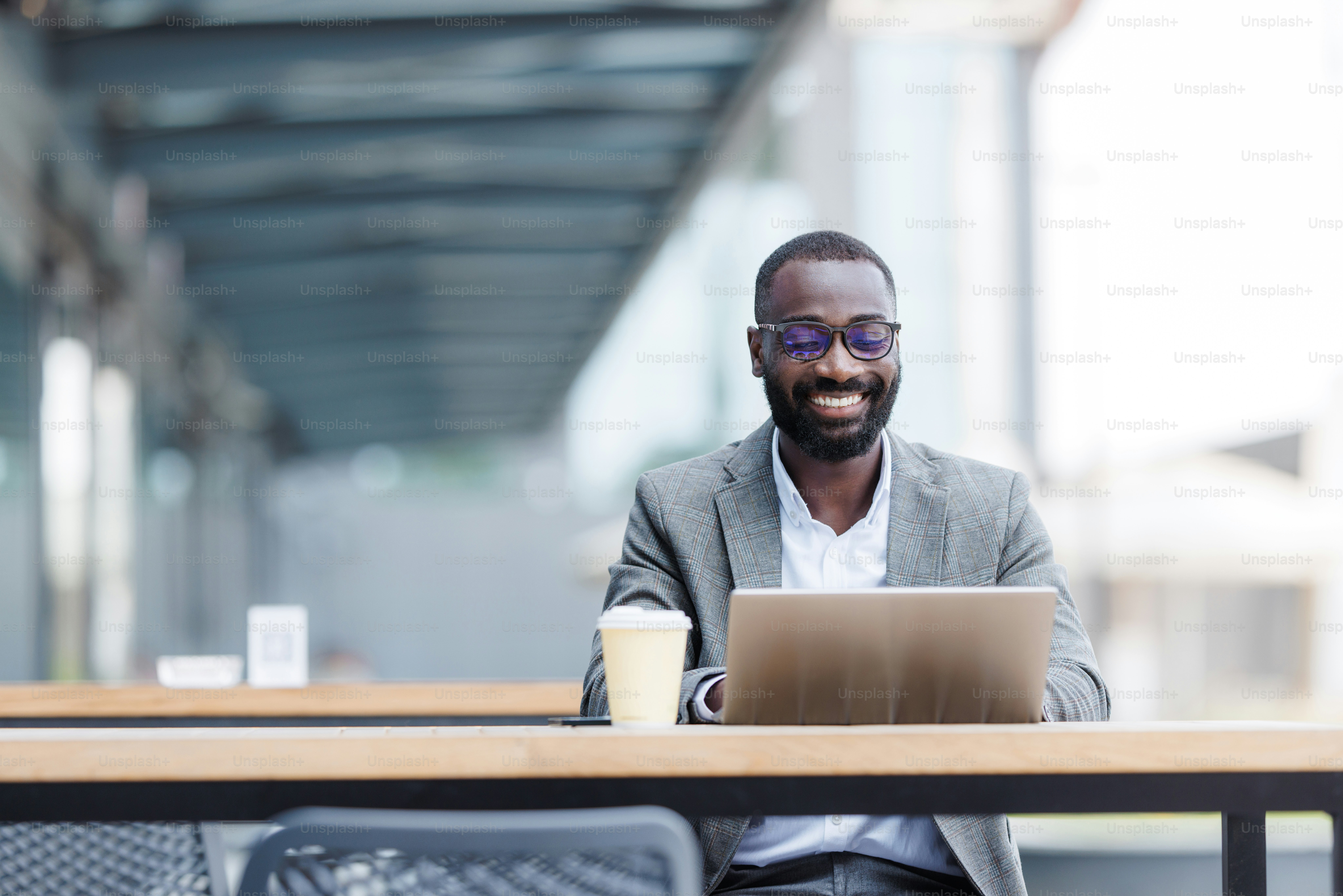 A confident businessman enjoys working on his laptop at an outdoor cafe, embodying productivity and modern work culture in a relaxed setting.