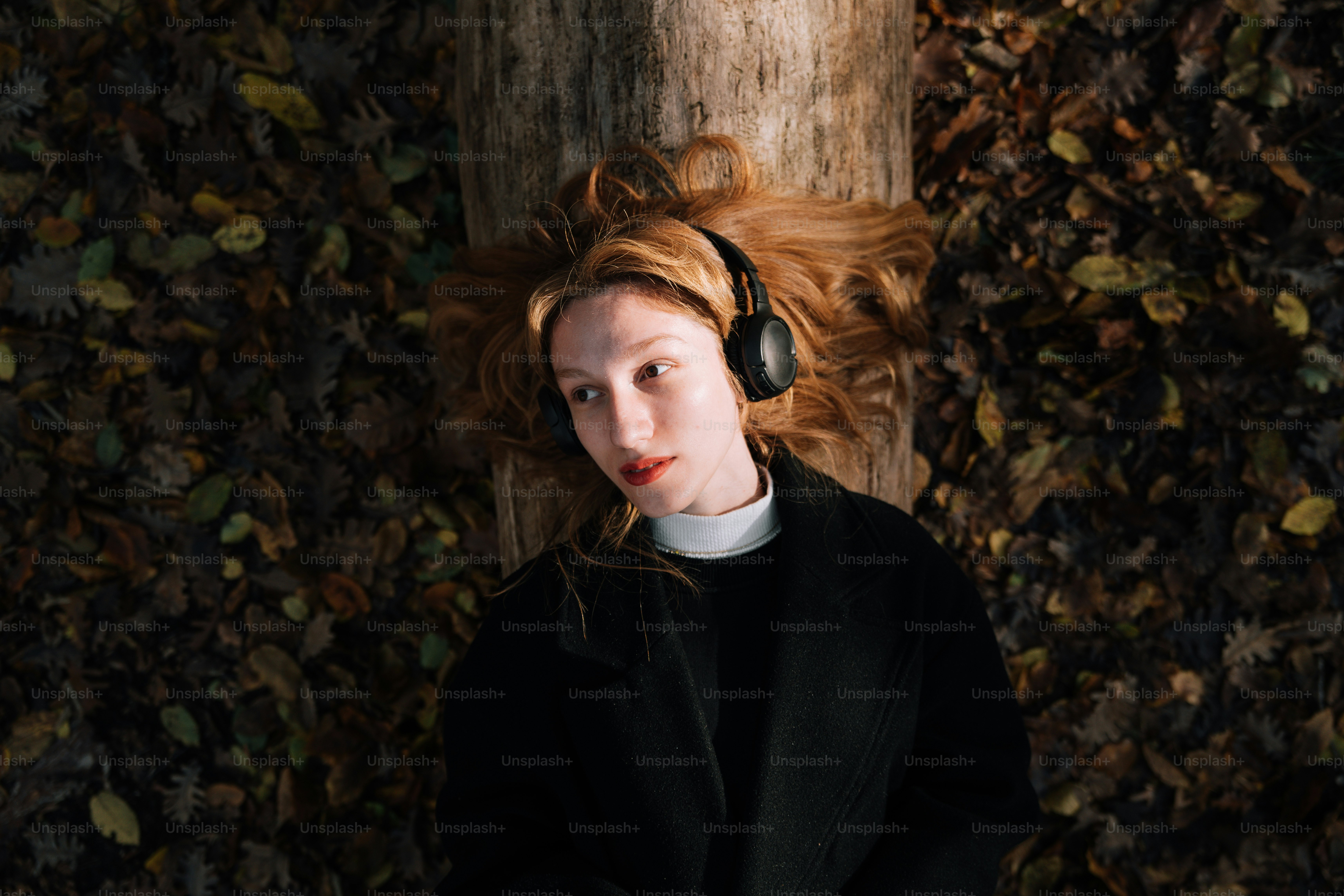A woman with headphones is leaning against a tree