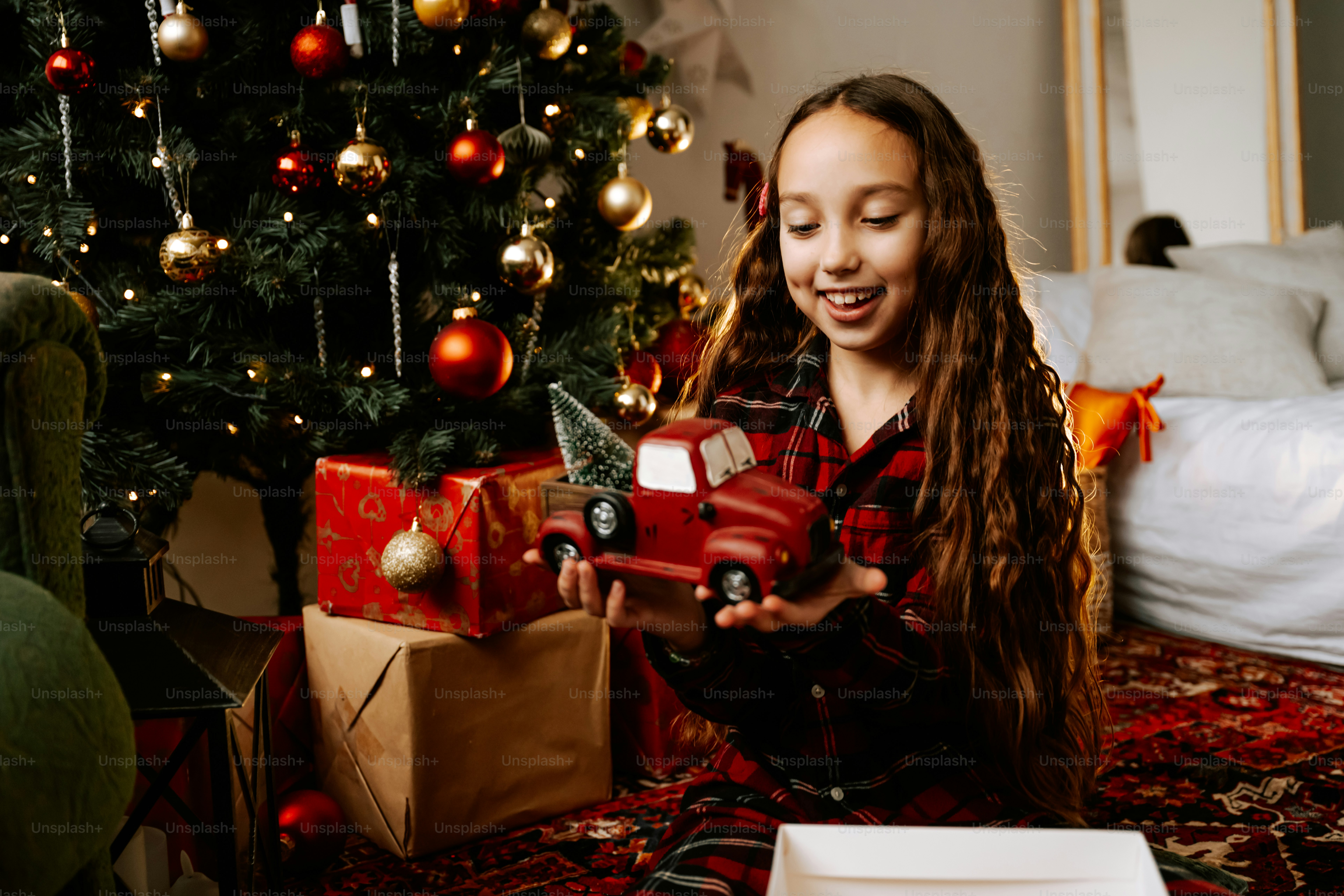 A young girl opening a christmas present in front of a christmas tree