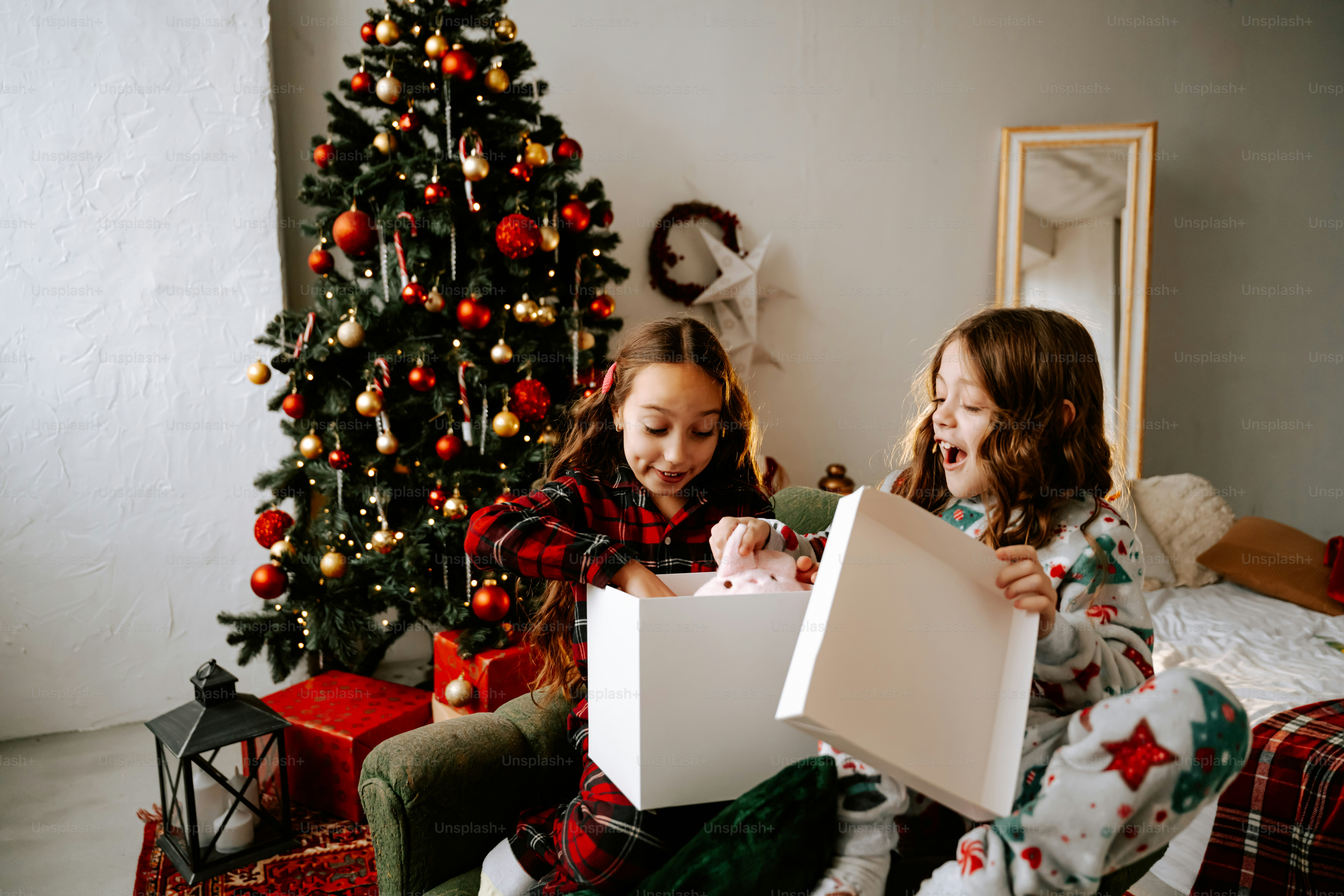 Two little girls sitting on a bed with presents in front of a christmas tree