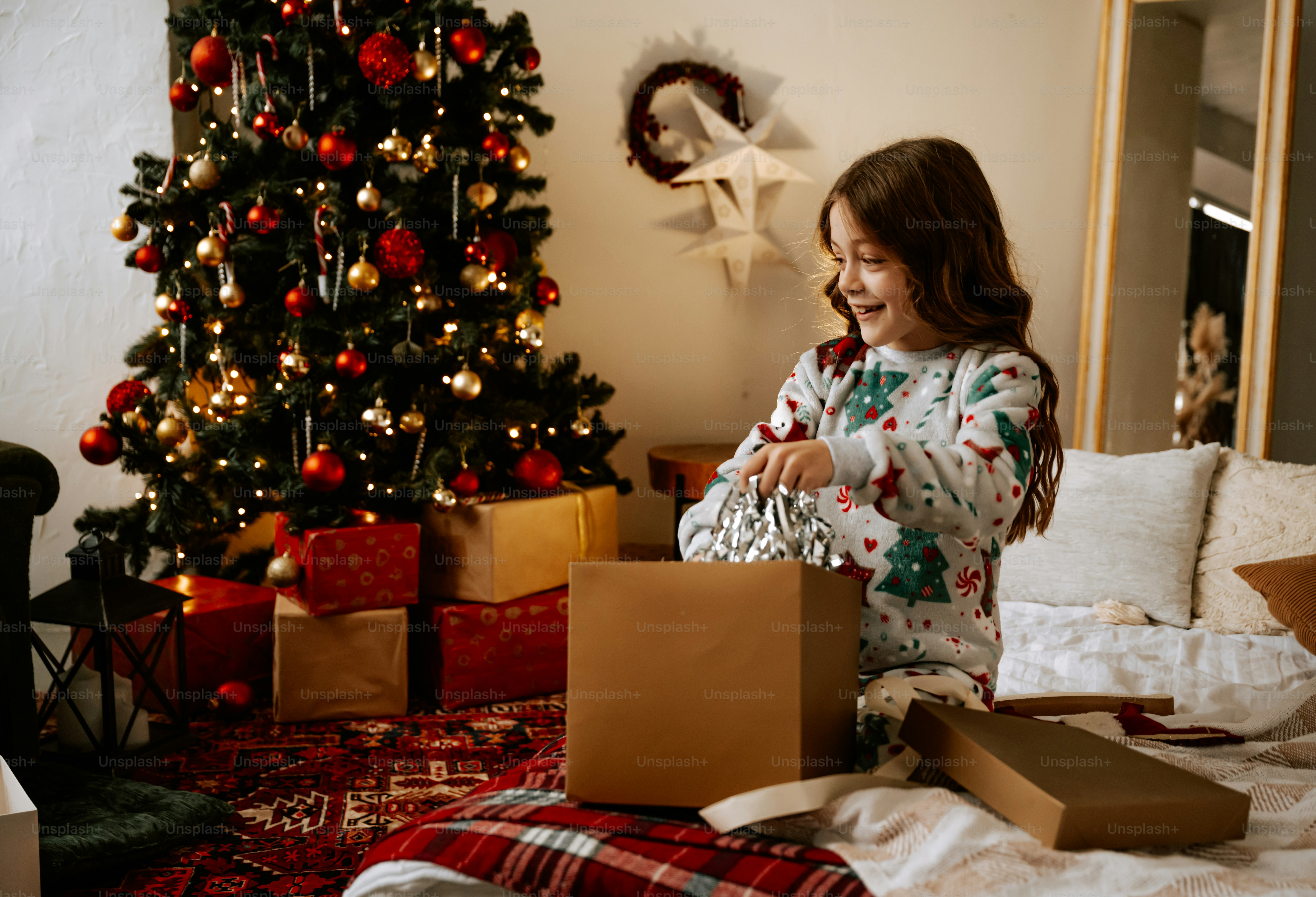 Una niña abriendo un regalo de Navidad frente a un árbol de Navidad