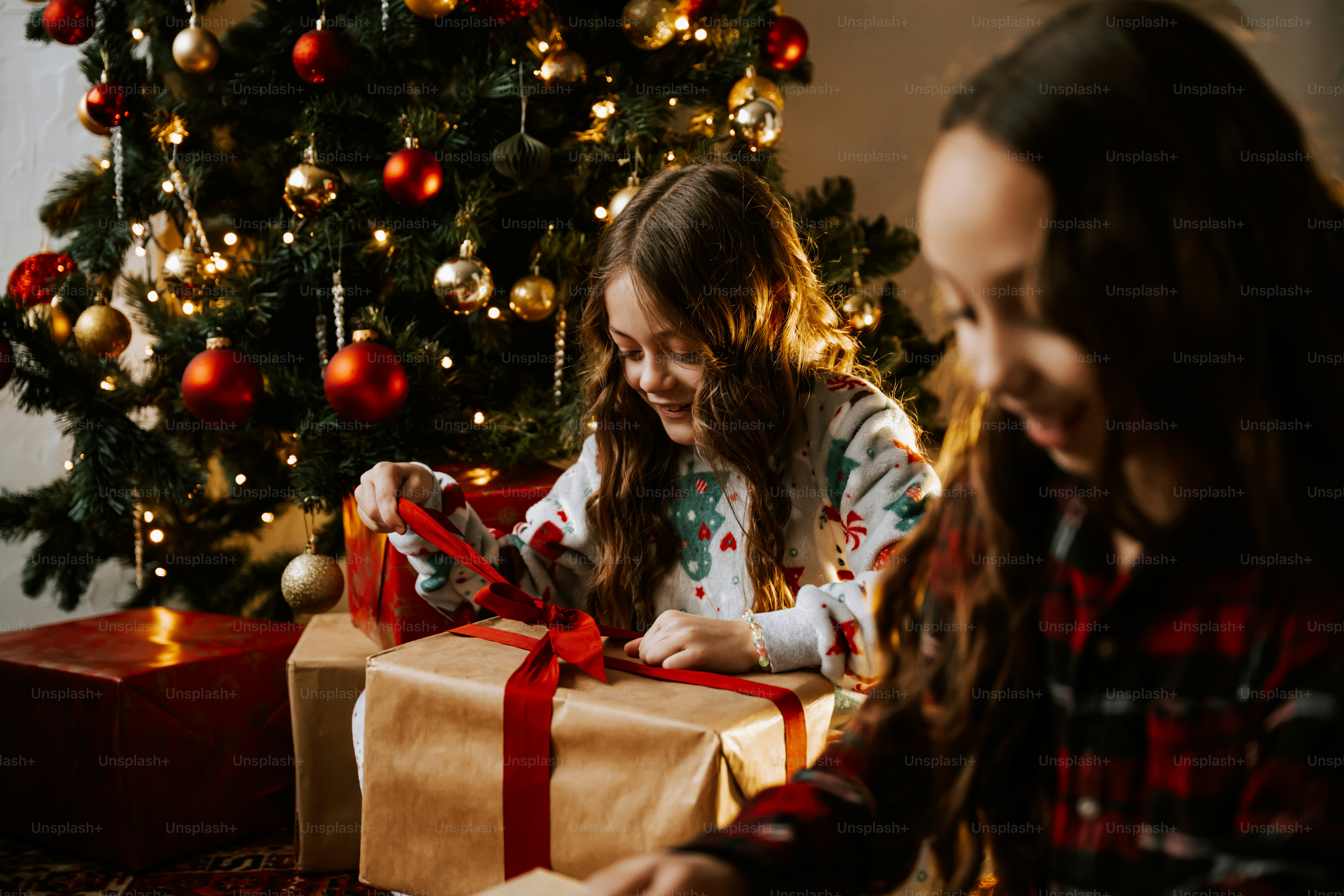 Two girls opening a christmas present in front of a christmas tree