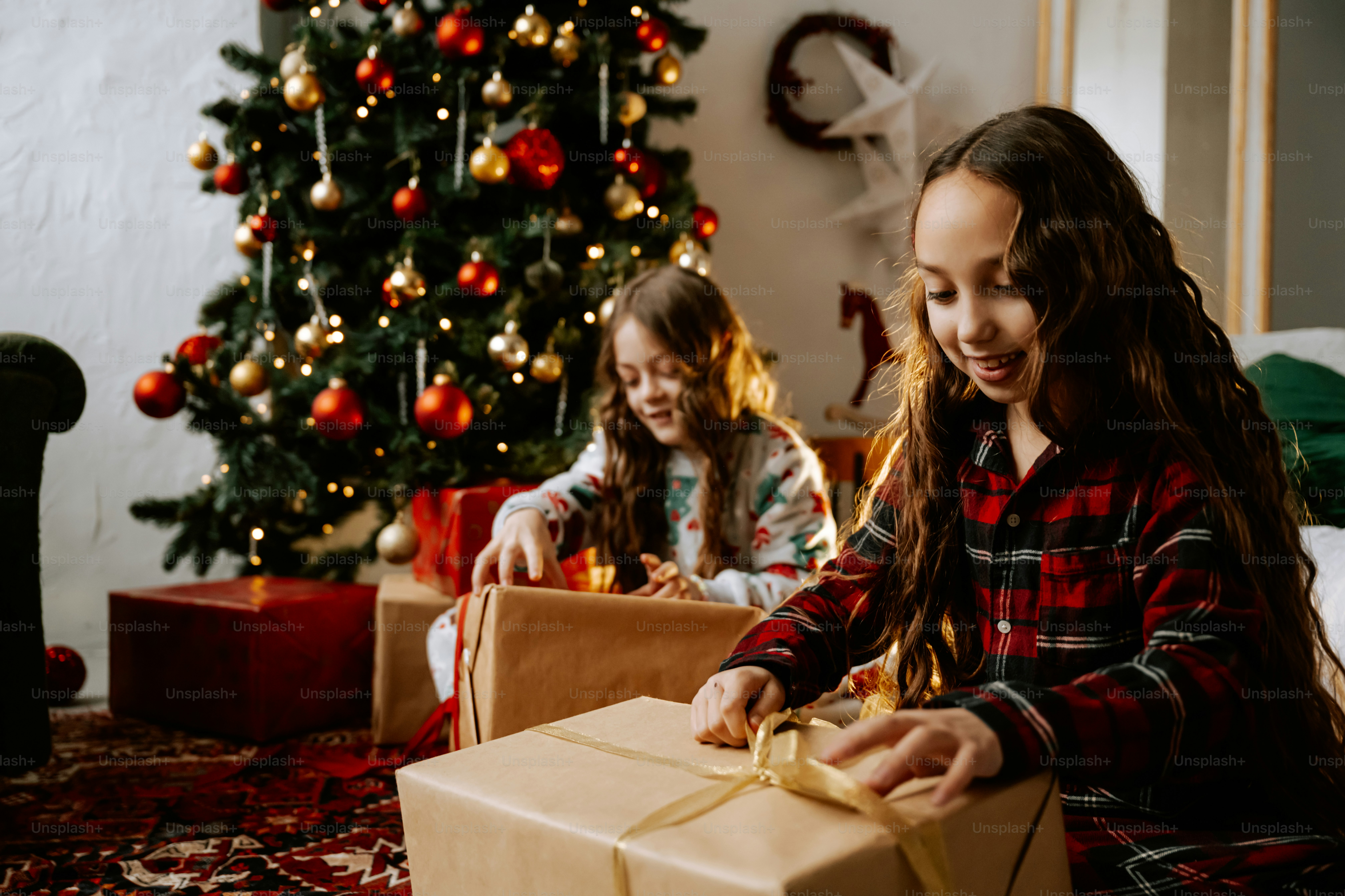 Two girls opening a christmas present in front of a christmas tree