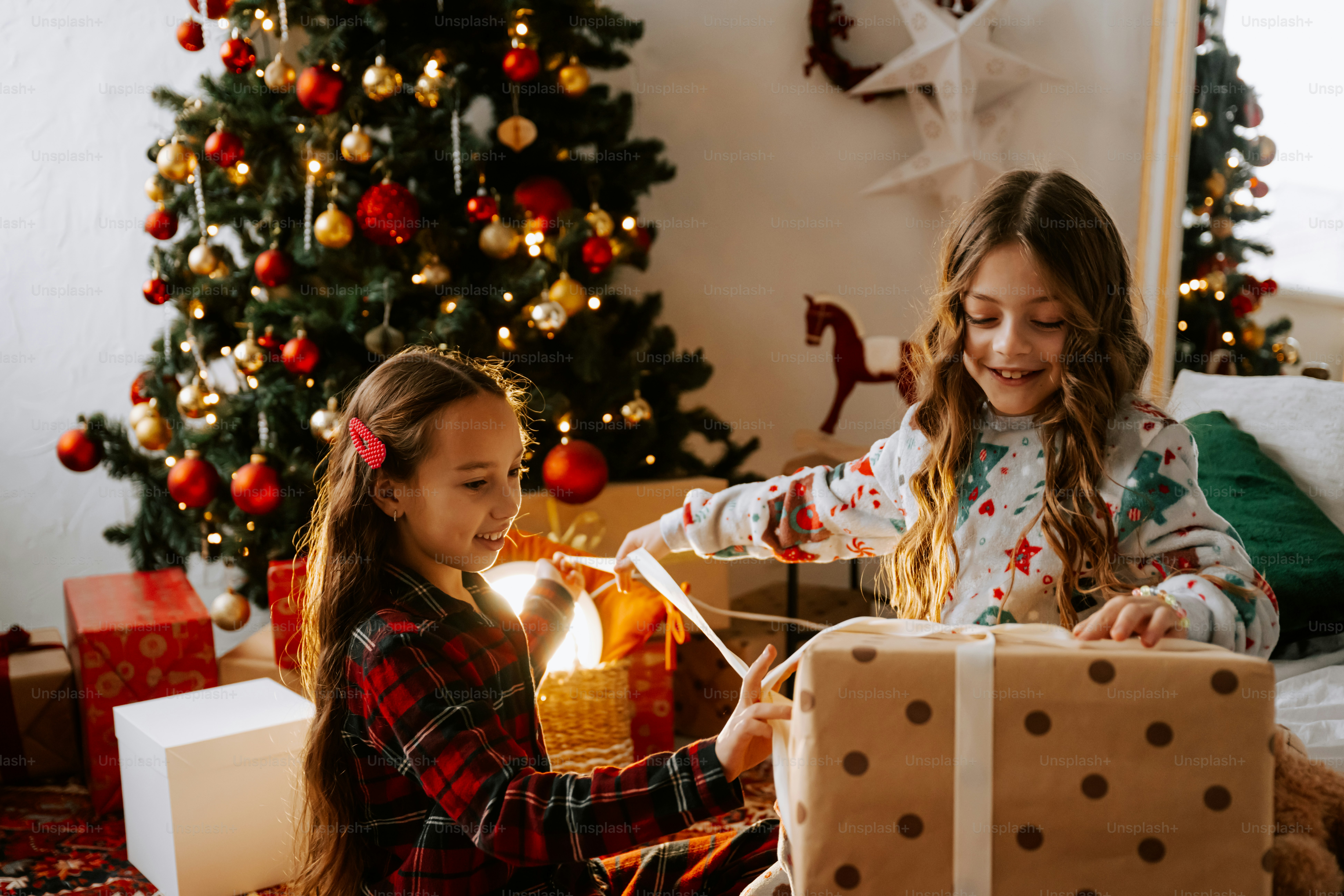 Two young girls opening presents in front of a christmas tree