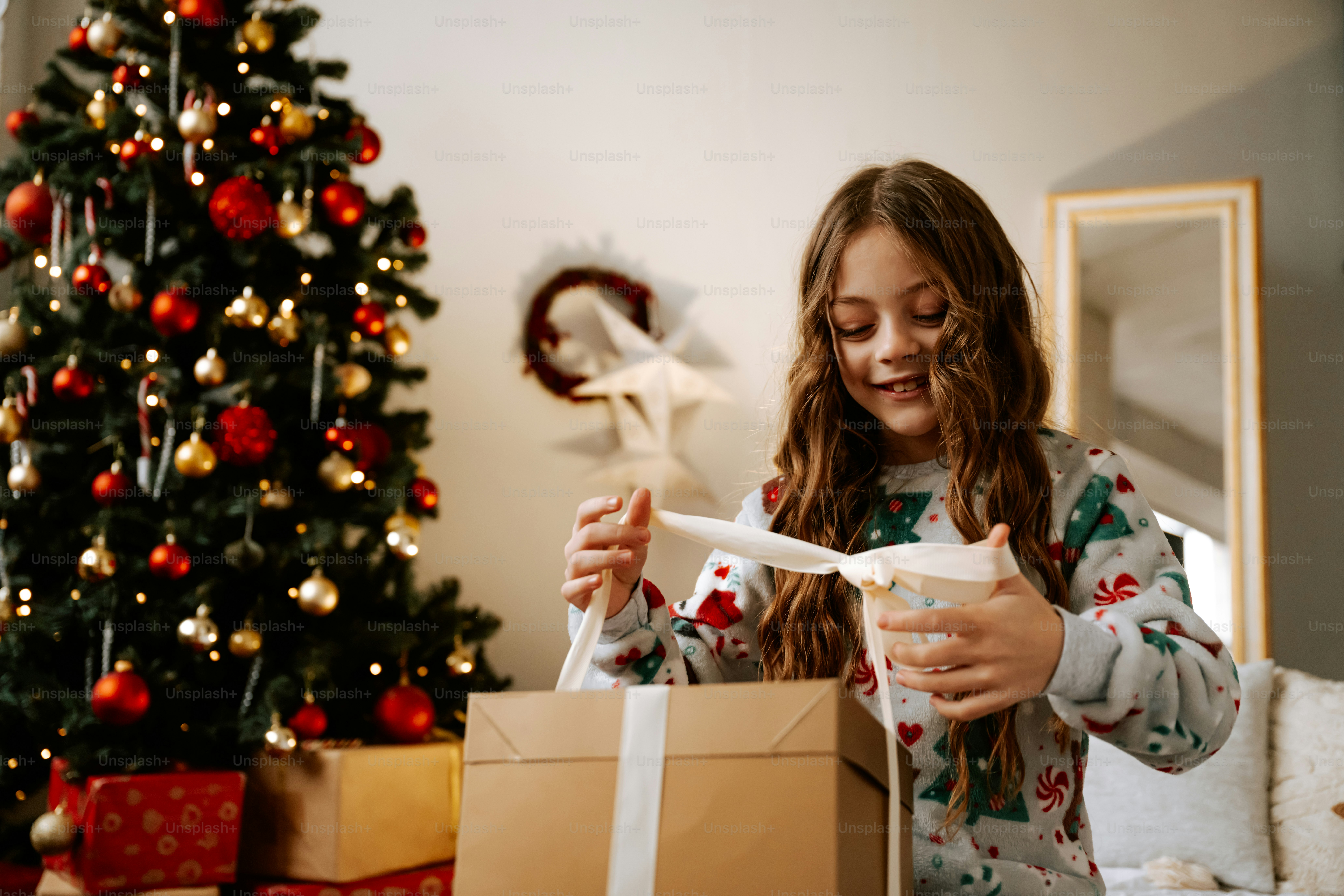 Une femme ouvrant un cadeau de Noël devant un sapin de Noël