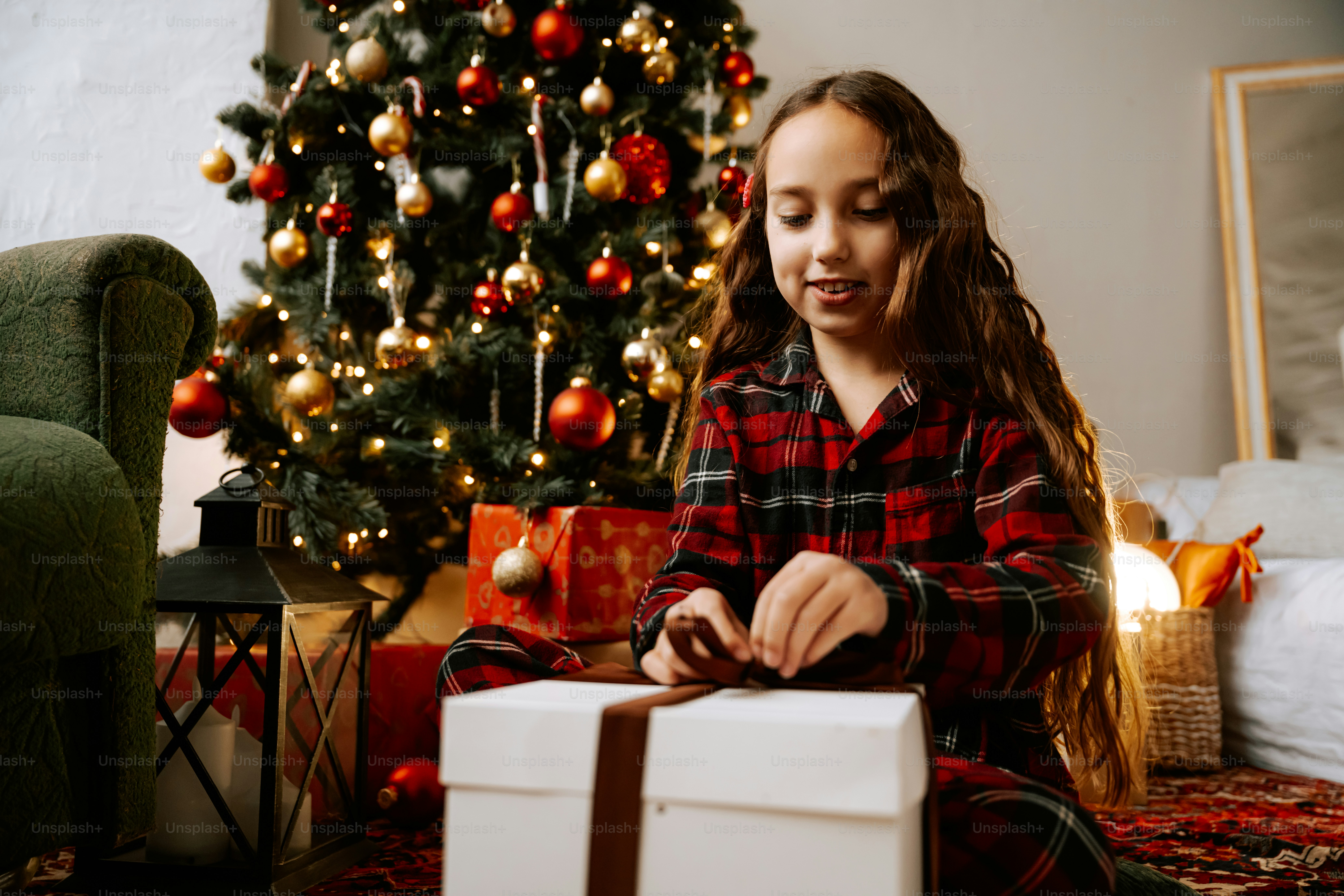 Ein junges Mädchen, das ein Weihnachtsgeschenk vor einem Weihnachtsbaum öffnet