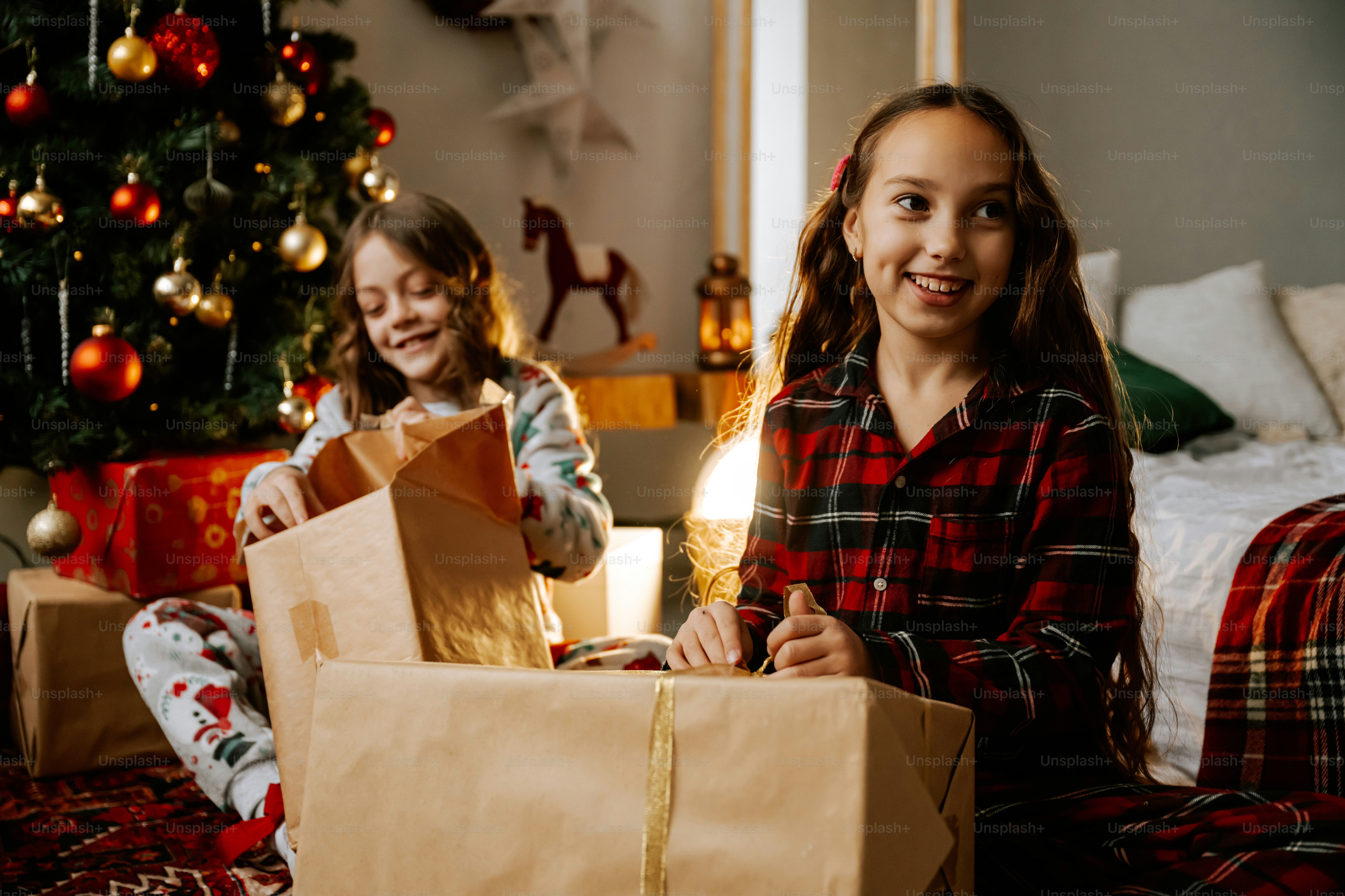 Two girls sitting on the floor with presents in front of a christmas tree