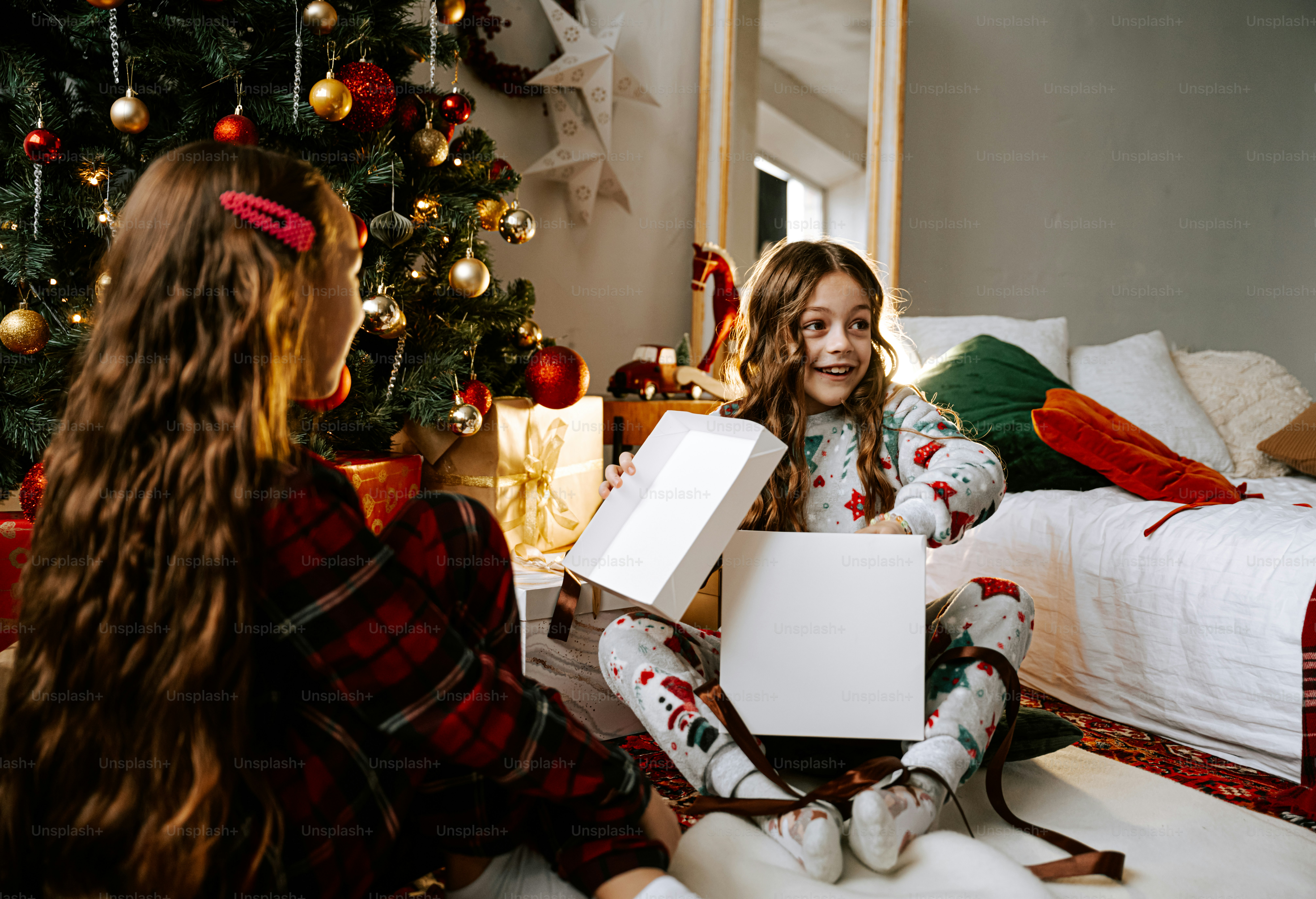 Deux filles assises sur le sol devant un sapin de Noël