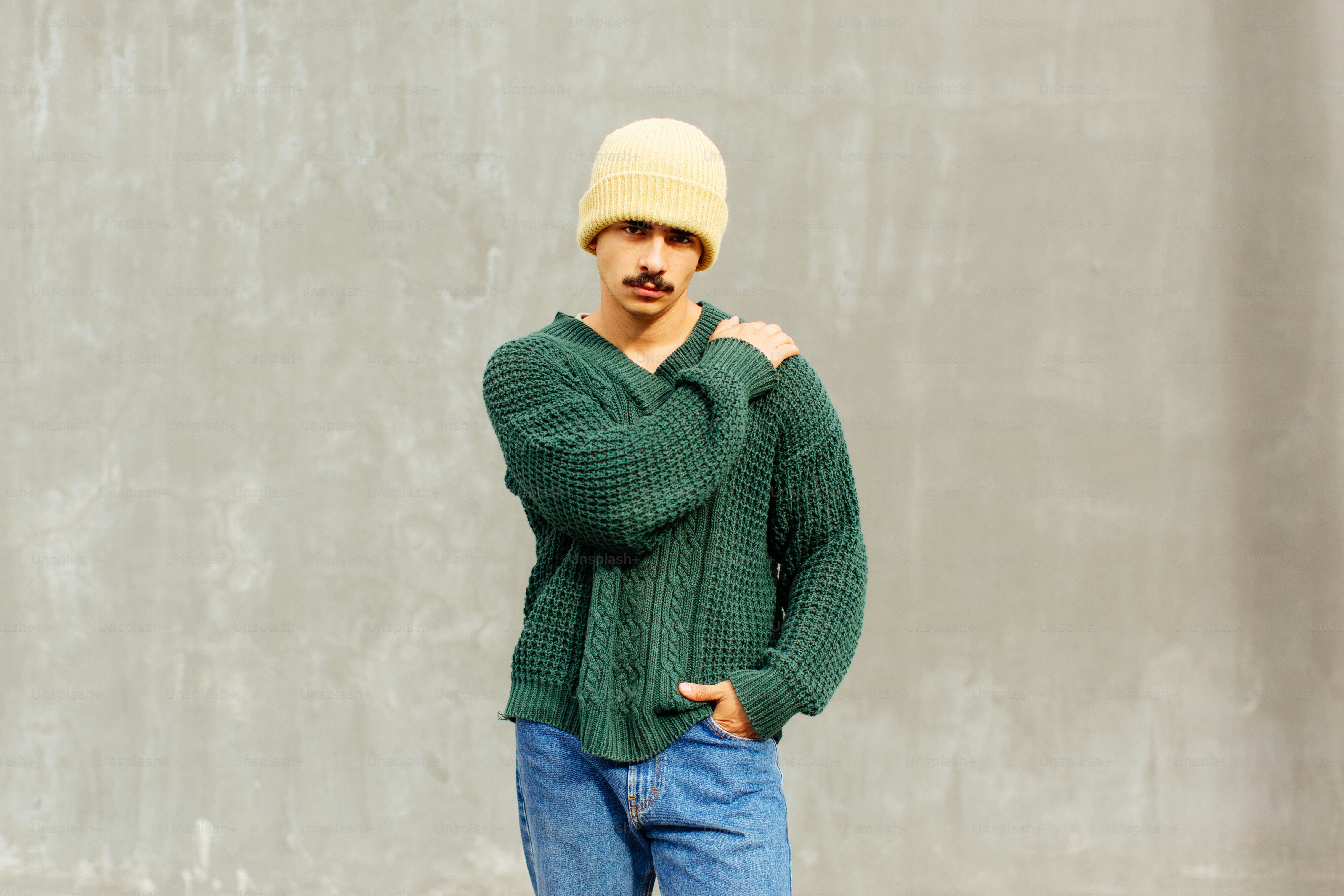 A man standing in front of a wall wearing a green sweater