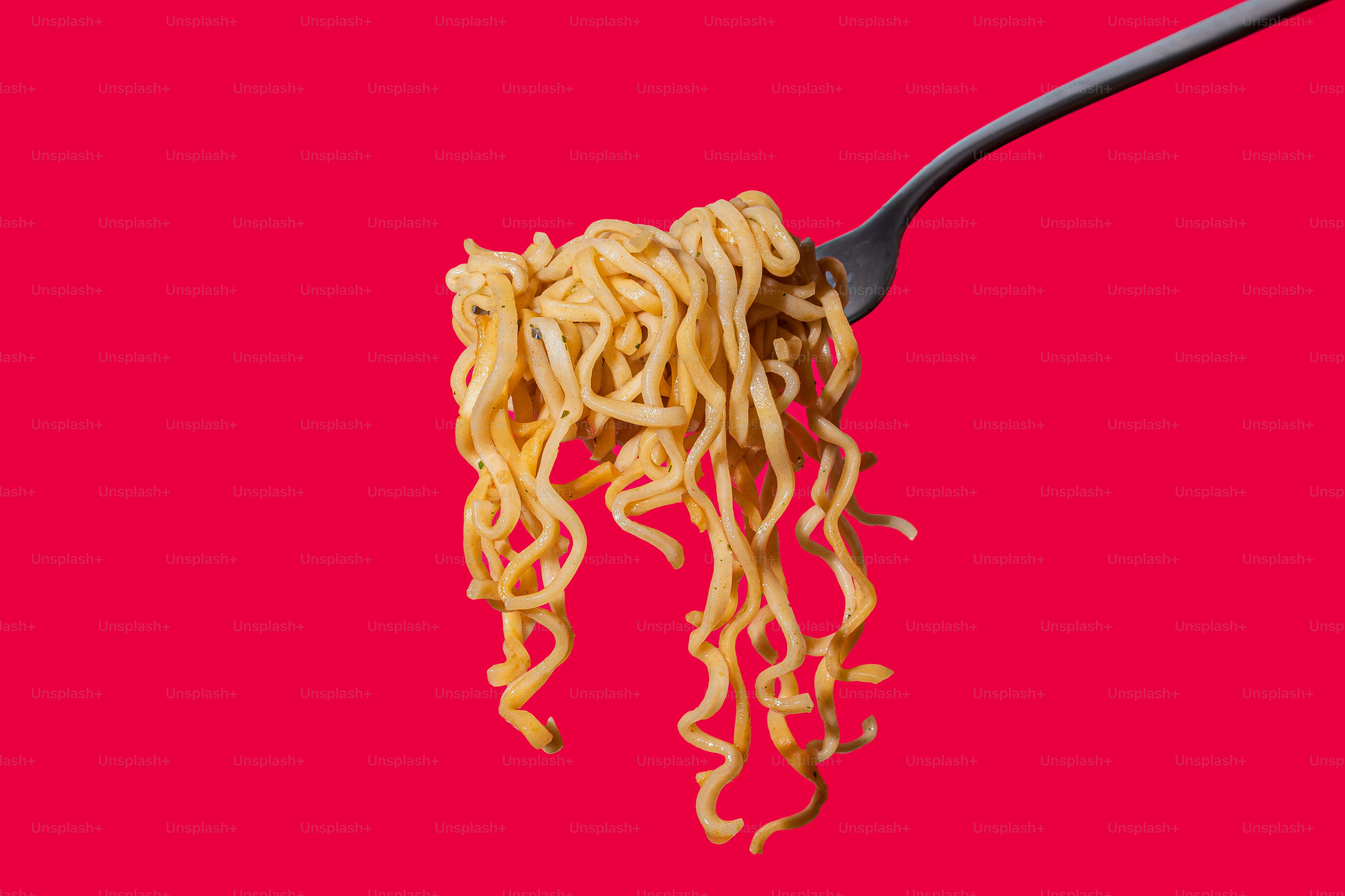 A spoon full of noodles on a pink background