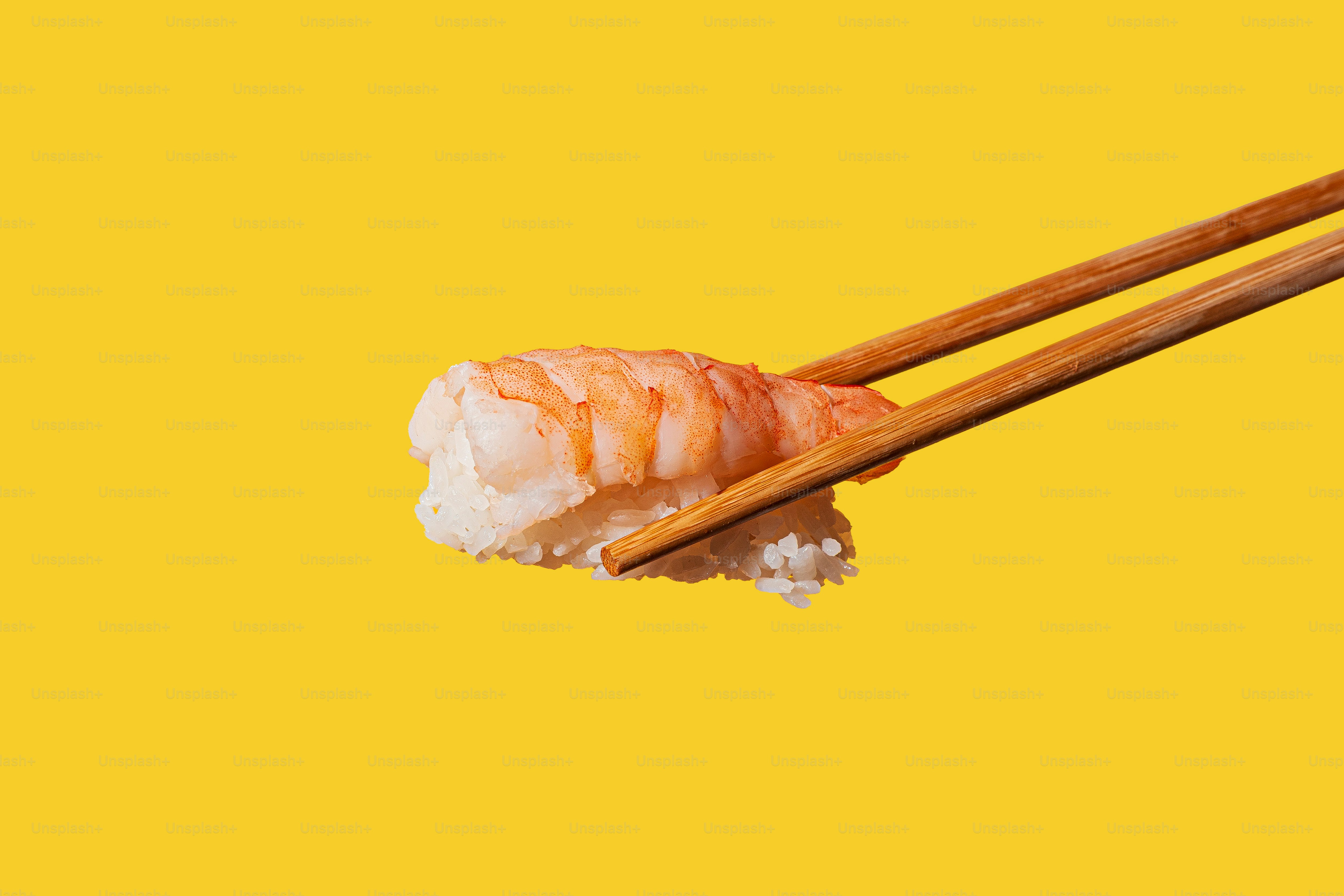 A pair of chopsticks with sushi on a yellow background