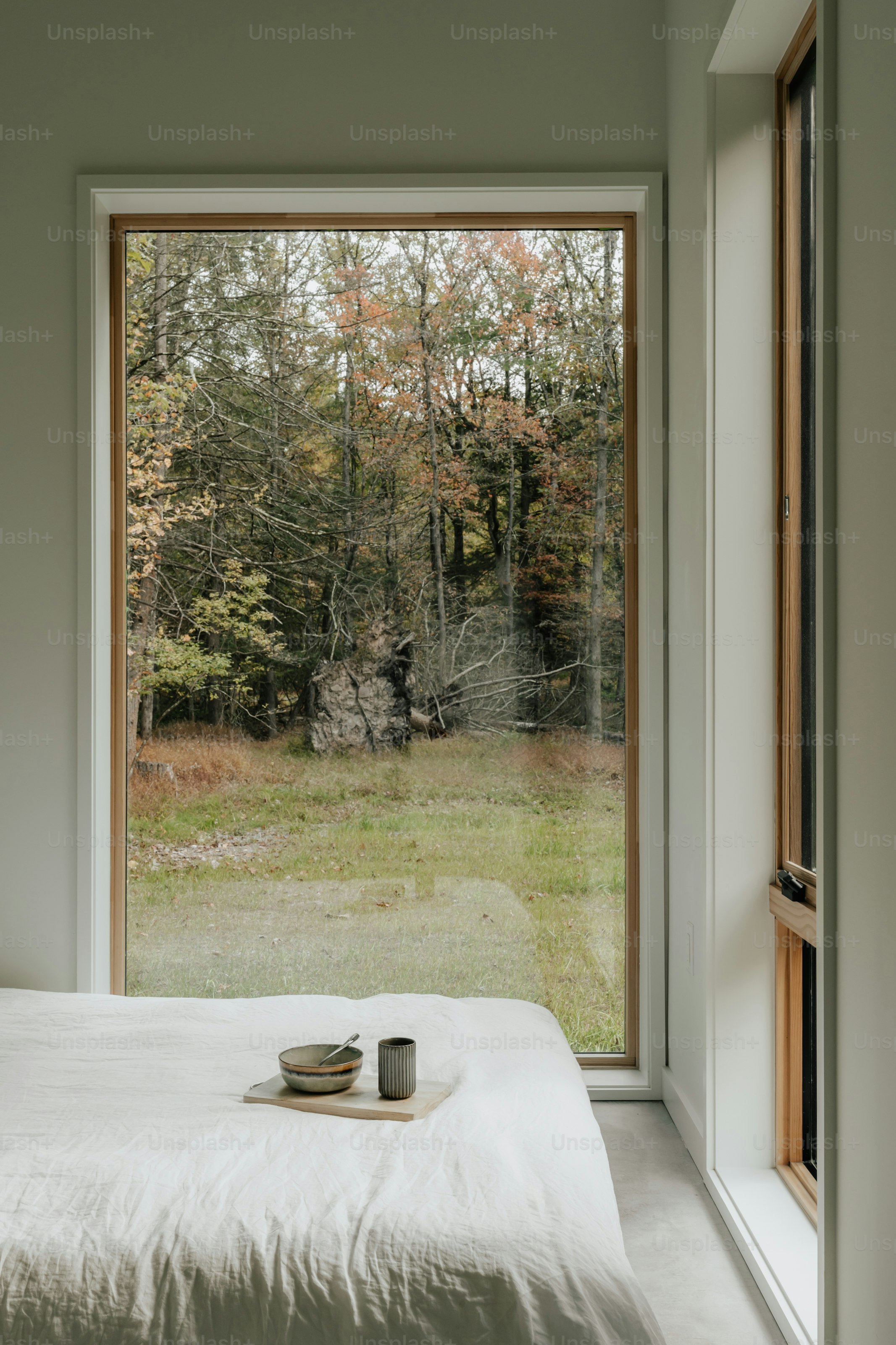 Une chambre avec une grande fenêtre et un lit blanc