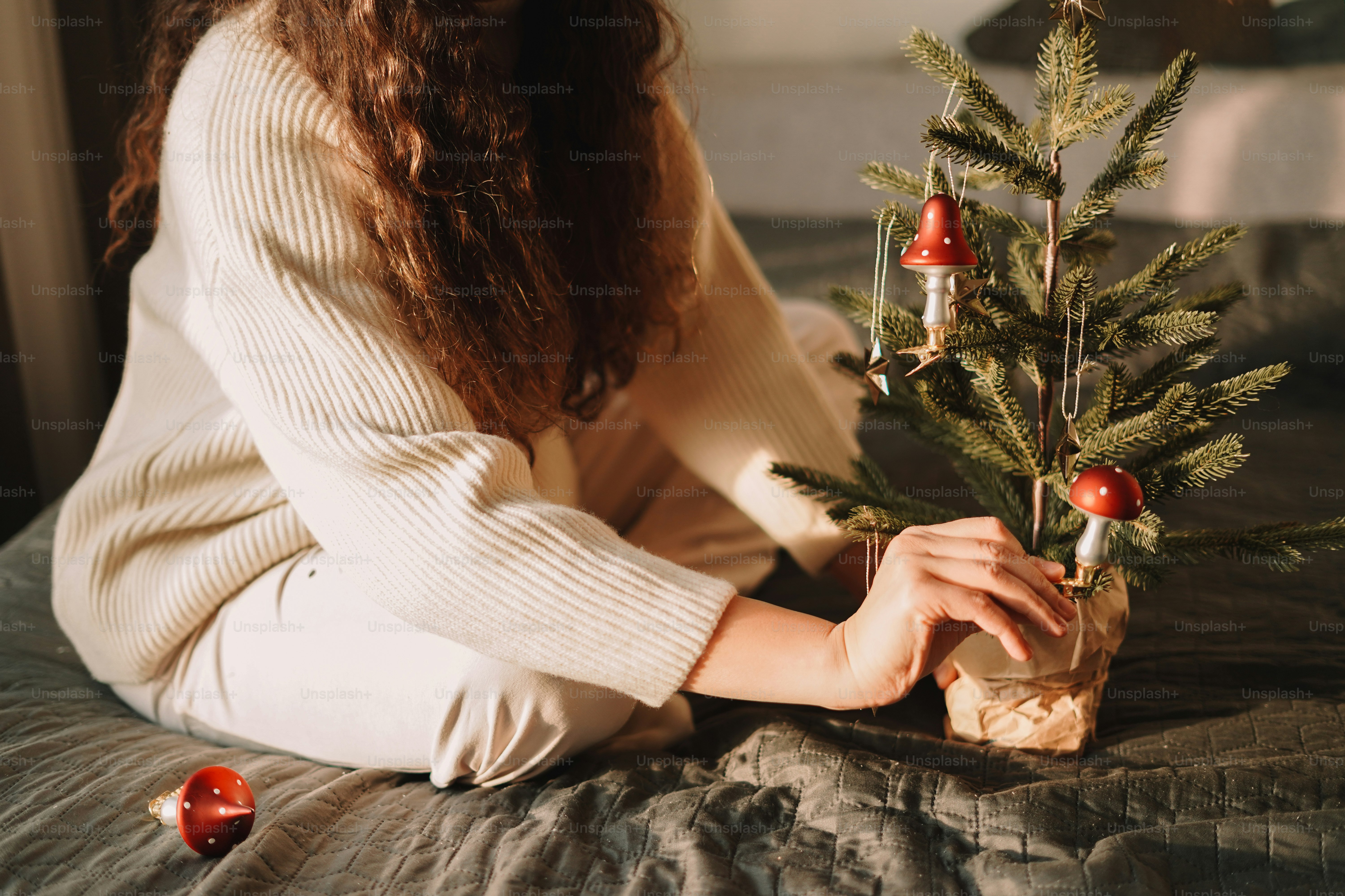A woman sitting on a bed holding a small christmas tree