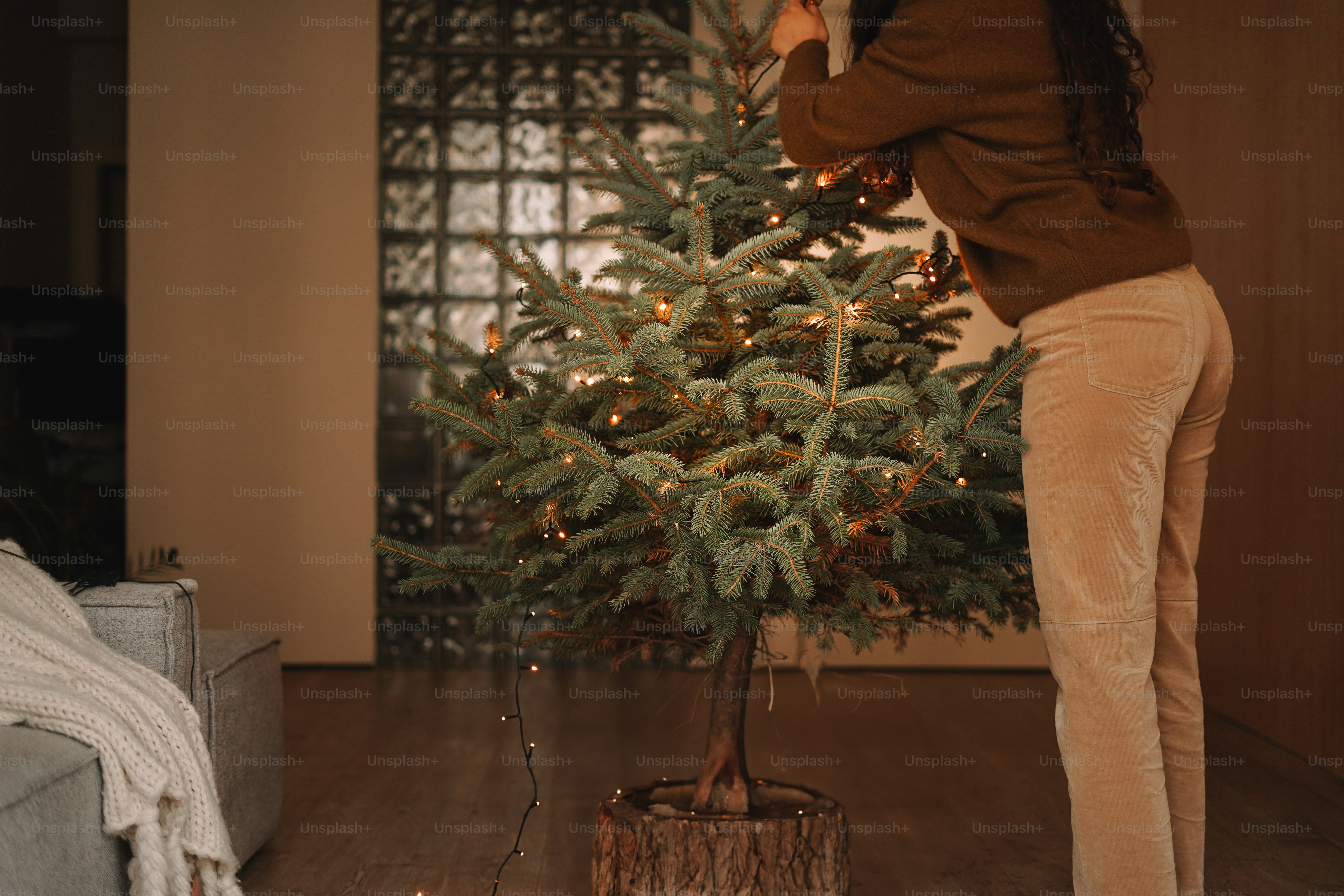 A woman putting lights on a christmas tree