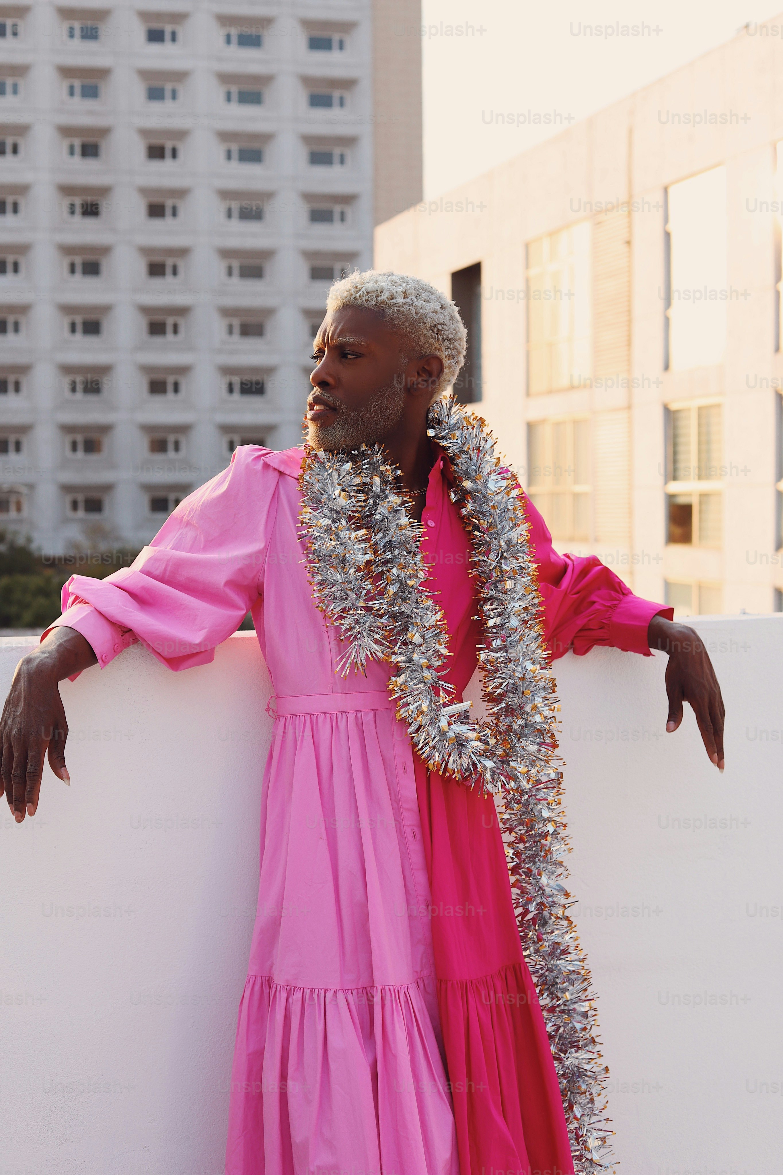 A man in a pink dress leaning against a white wall